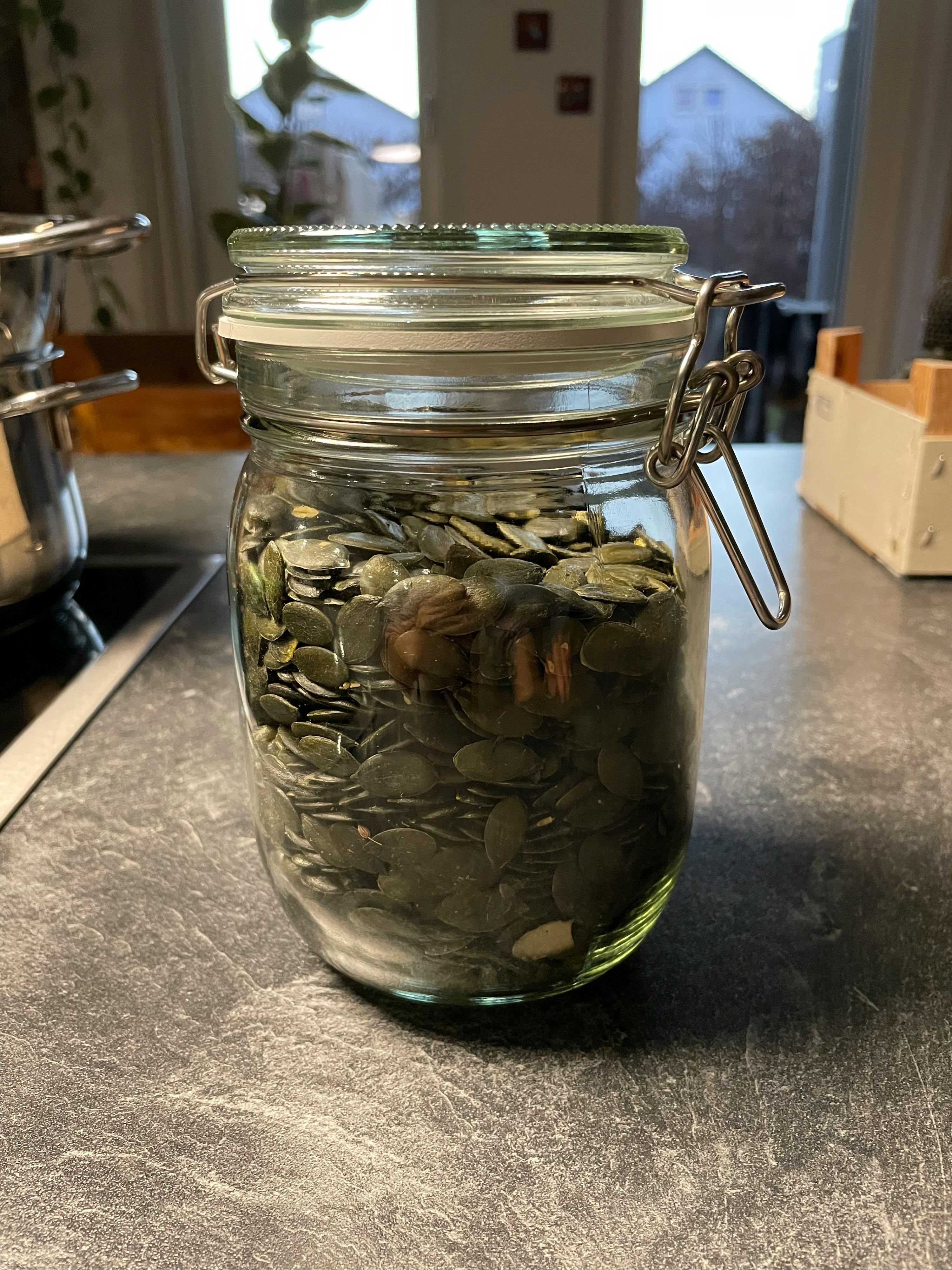 a jar filled with pumpkin seeds sits on a counter