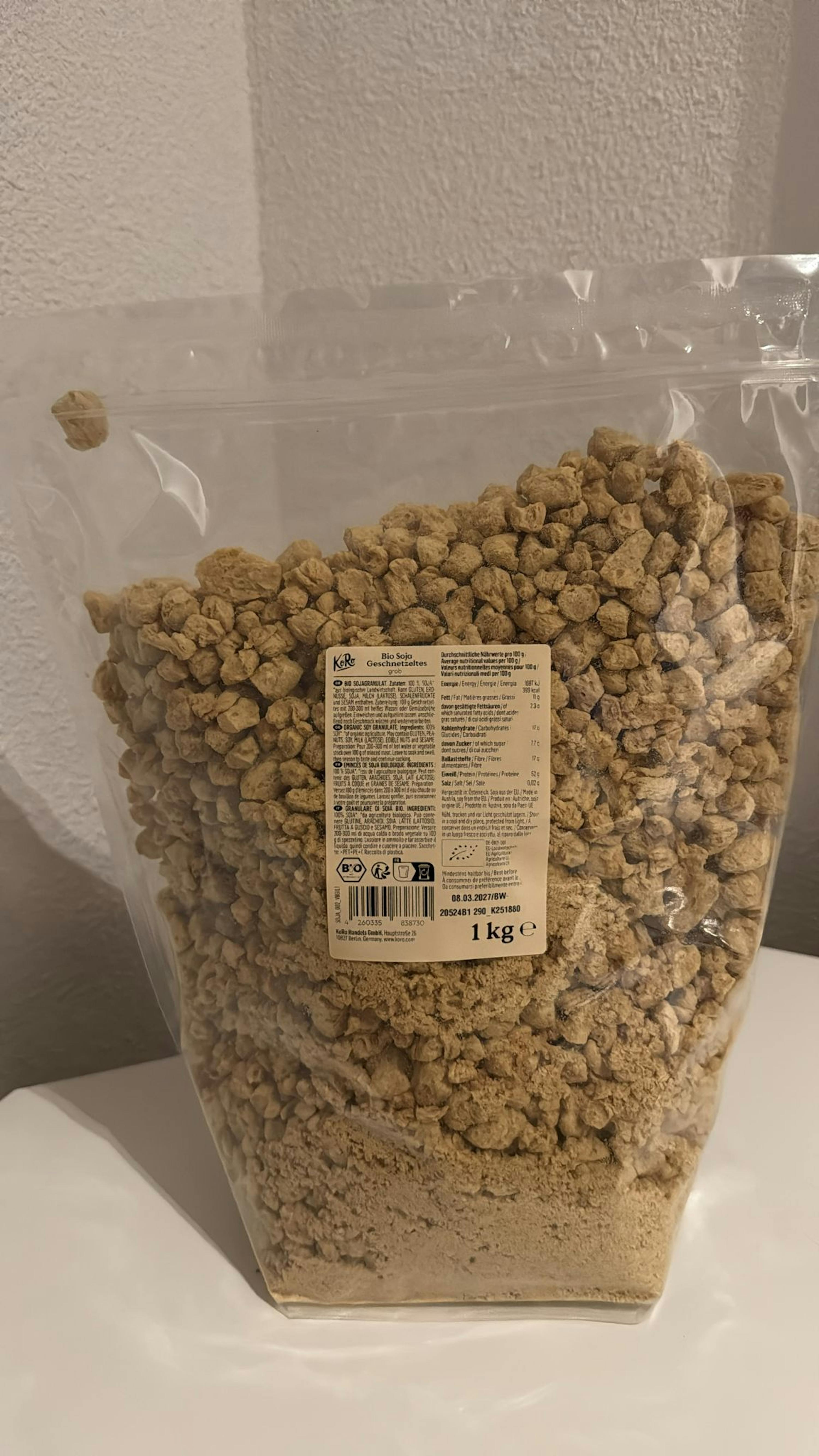 un sac en plastique transparent rempli de granulés de soja bio de 1 kg, avec une étiquette d'information visible.