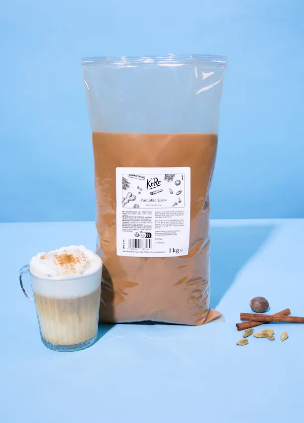 un grand sac d'épices pour citrouille, un latte aux épices pour citrouille et des épices entières (muscade, cannelle, cardamome) sont présentés sur un fond bleu.