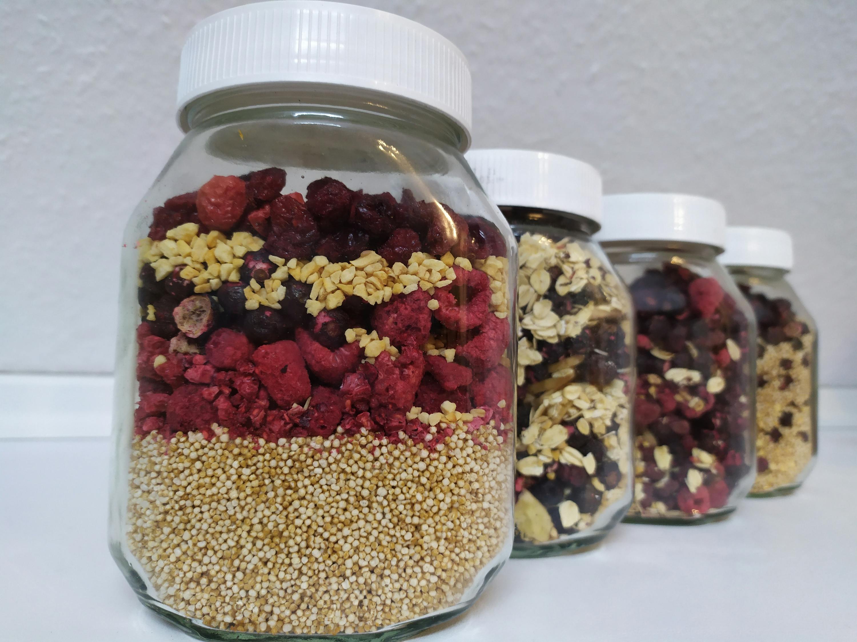 quatre bocaux en verre remplis de granola et de fruits séchés