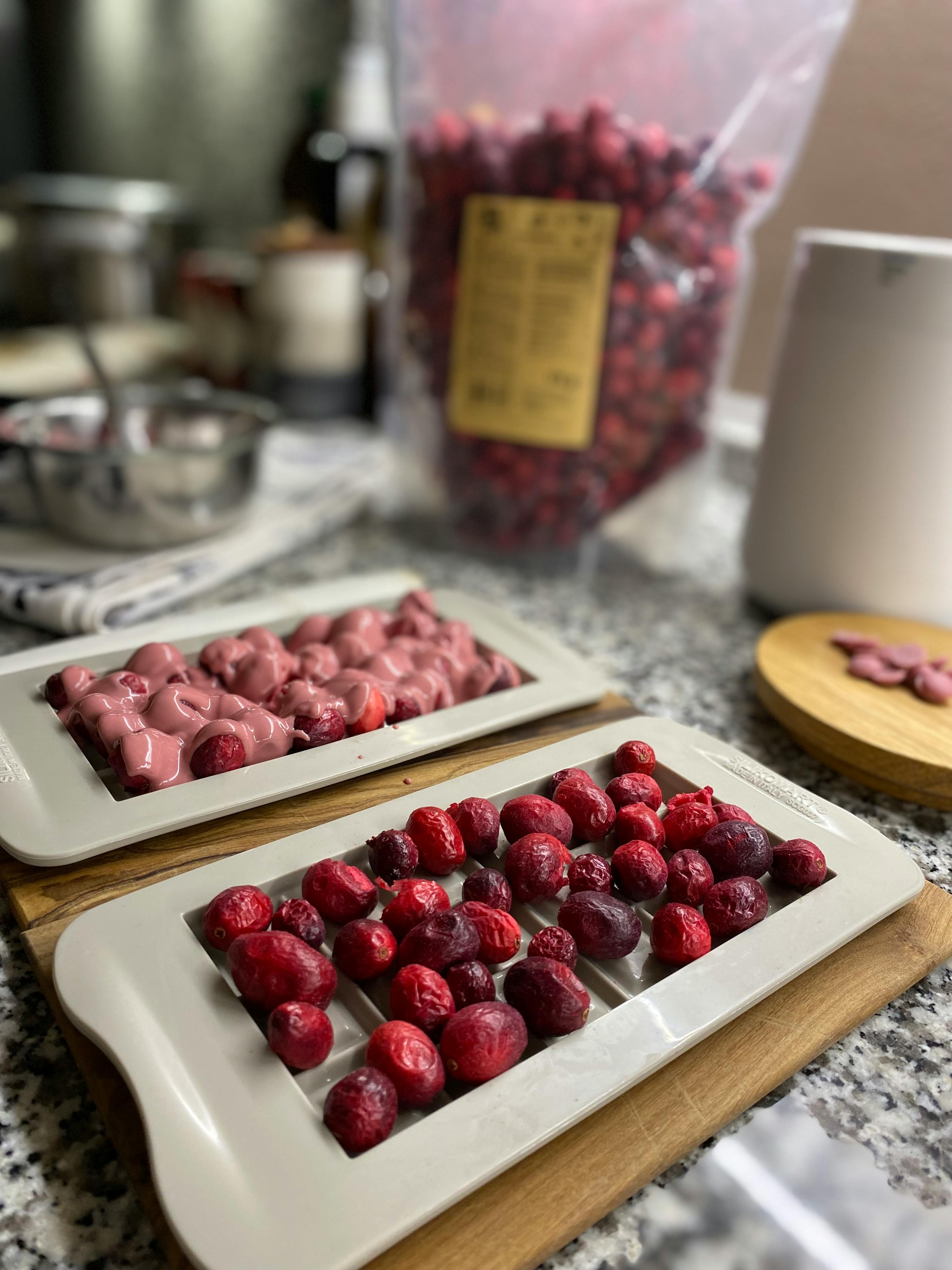 a bag of dried cranberries sits on a counter next to two trays of cranberries