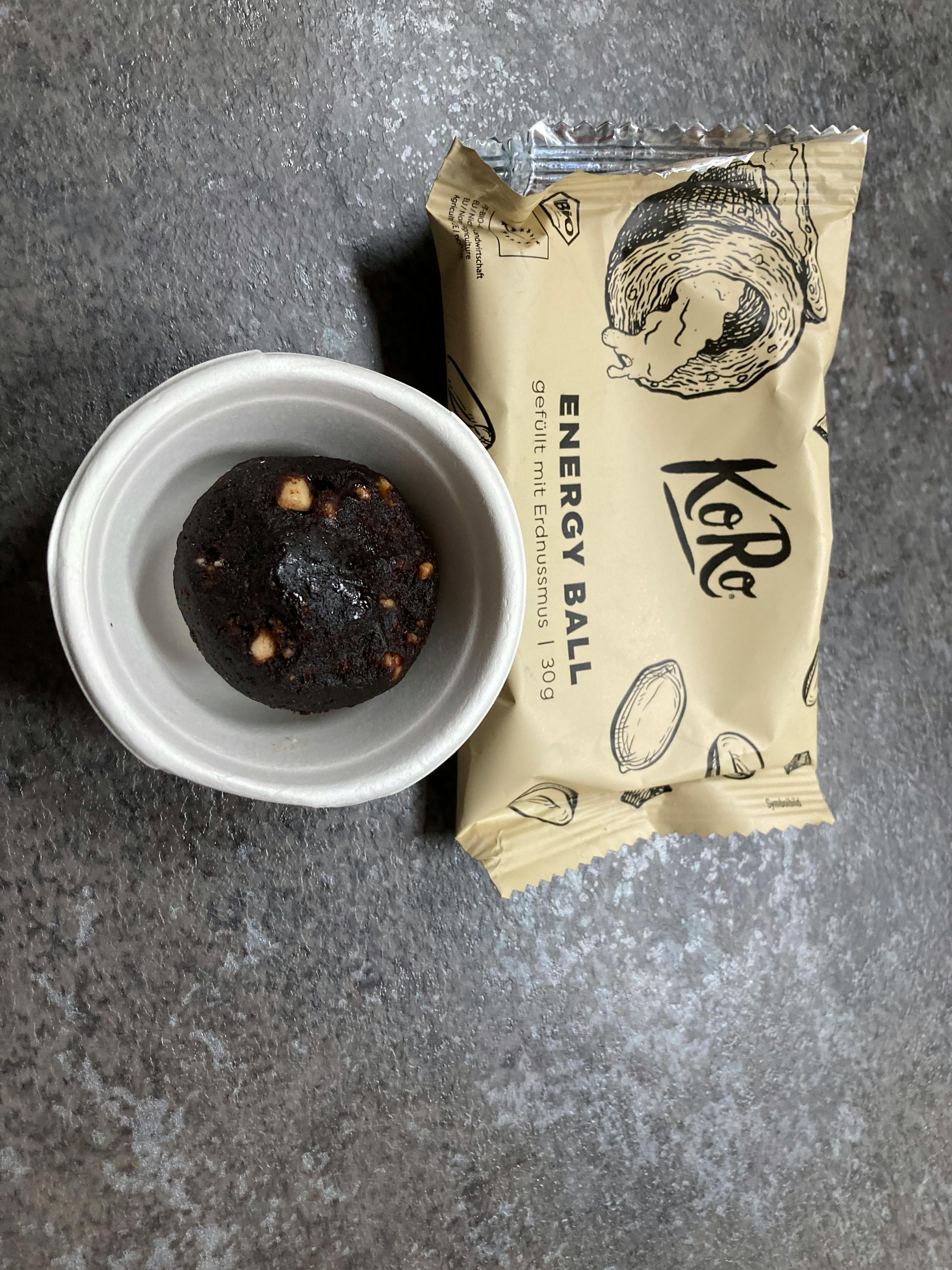 eine kleine weiße Schüssel mit einem braunen Ball neben einer Tüte mit einem braunen Ball darauf