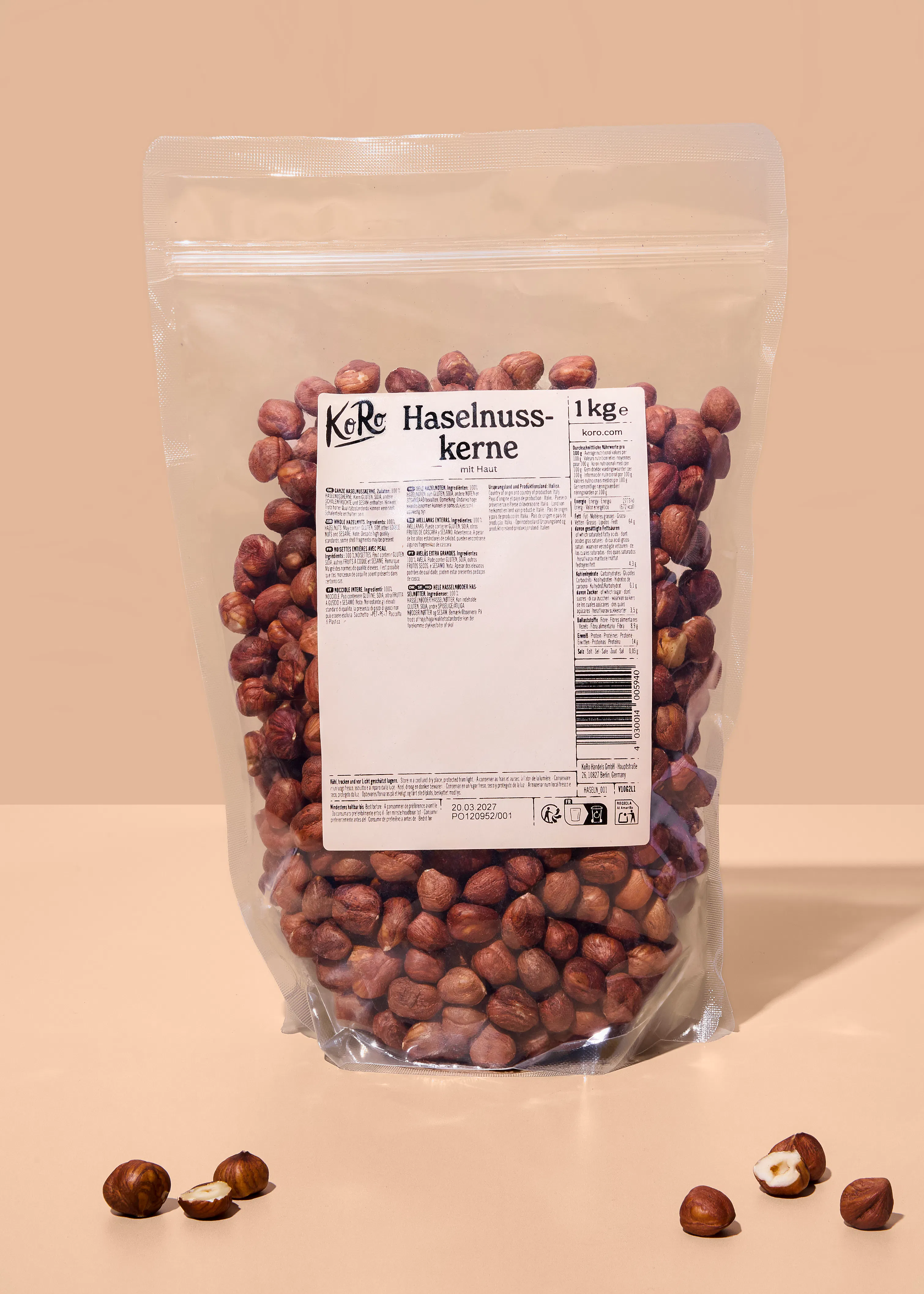 eine transparente verpackung von koro haselnusskernen mit haut, 1 kg, steht auf einer hellen oberfläche, mit einigen losen haselnüssen daneben.