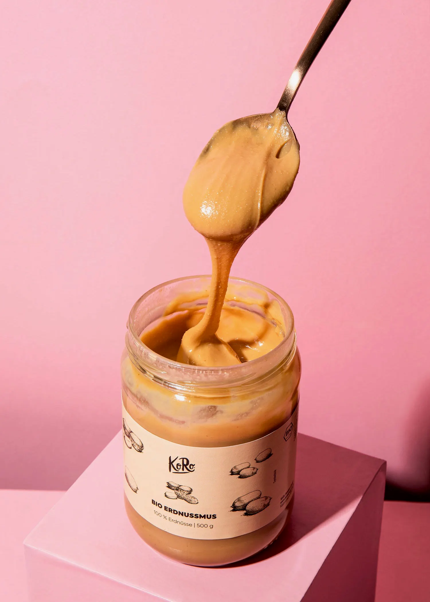ein Glas Erdnussmus wird mit einem Löffel aus dem Glas geschöpft