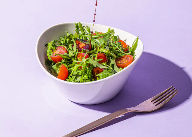 un bol blanc rempli de tomates et de roquette avec une fourchette