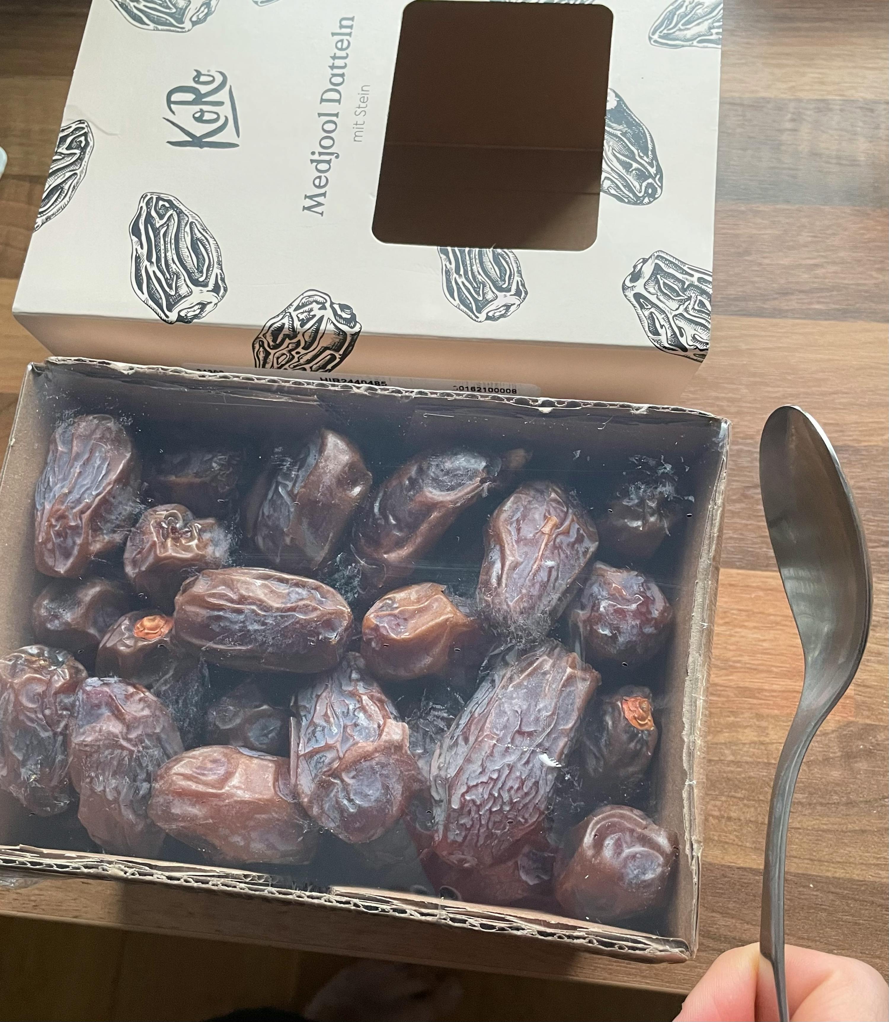 a box of medjool dates sits on a wooden table next to a spoon