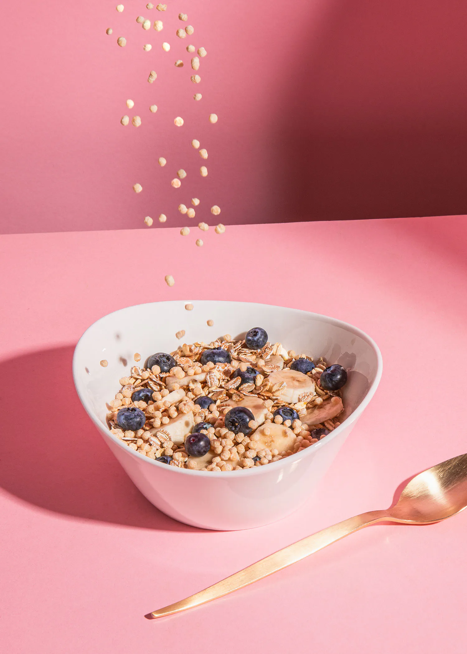 un bol de granola avec des bleuets et une cuillère sur une table rose