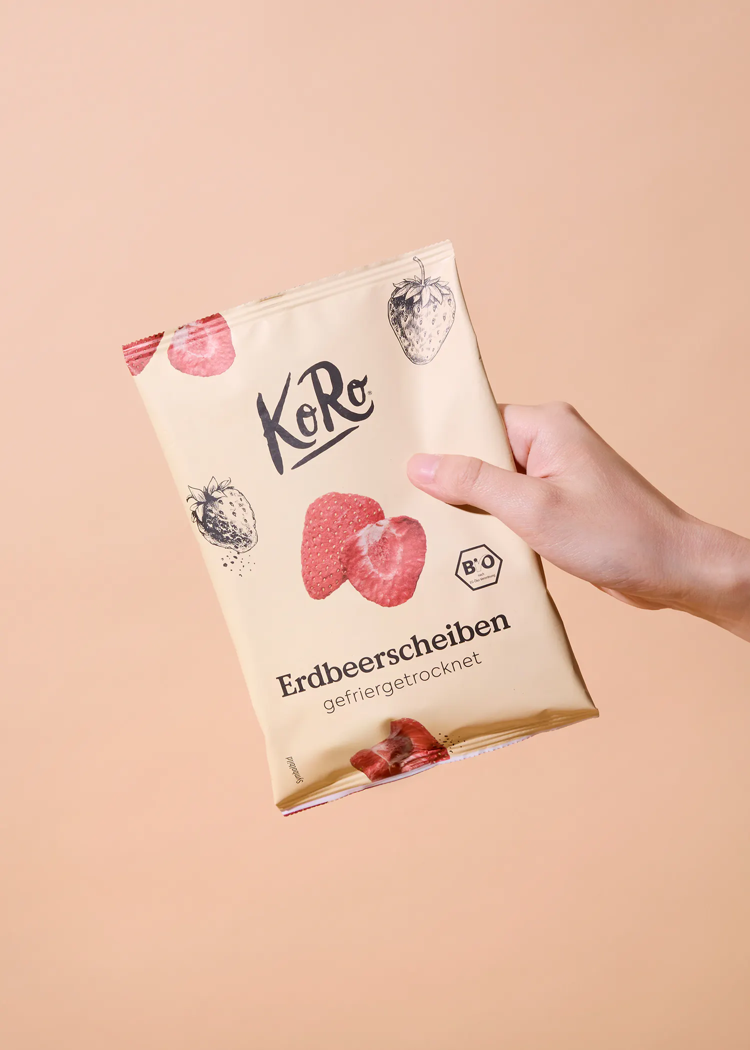 a hand holds a light yellow package of koro freeze-dried strawberry slices, featuring strawberry illustrations and the brand logo.