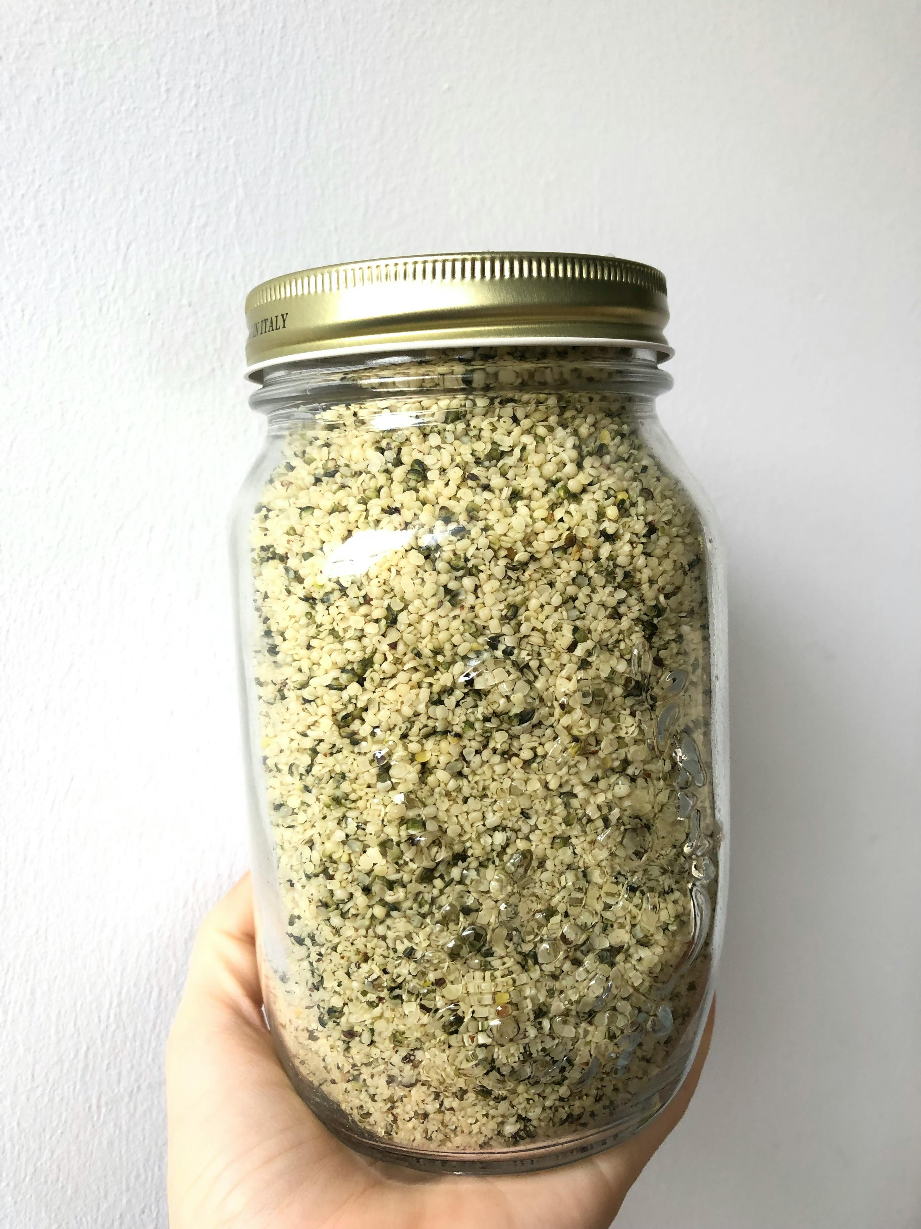 eine Person hält ein Glasgefäß mit Hanfsamen darin