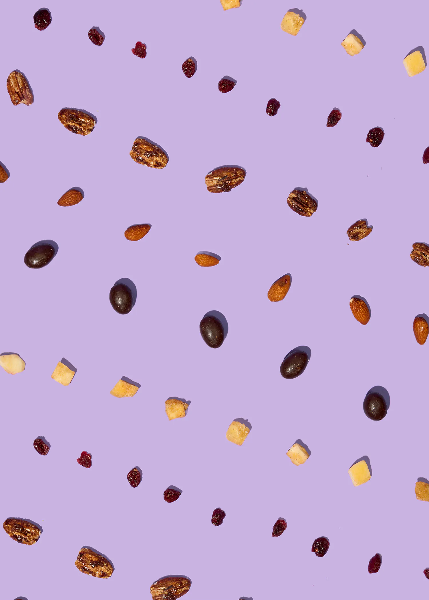 une variété de noix de pécan, d'amandes, de canneberges séchées, de morceaux de fruits tropicaux séchés et d'amandes enrobées de chocolat est dispersée sur un fond violet.