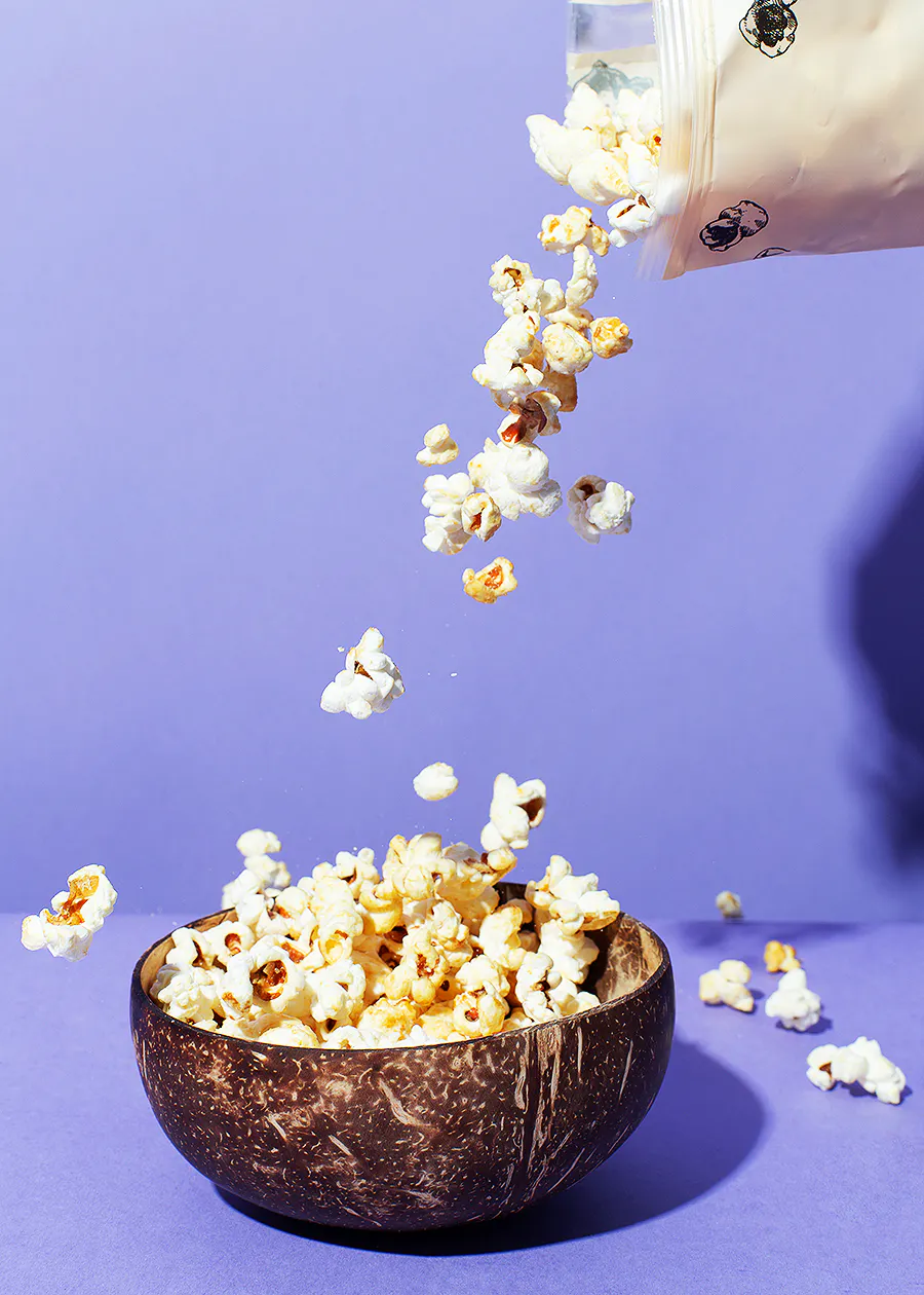 une personne verse du pop-corn dans un bol de noix de coco