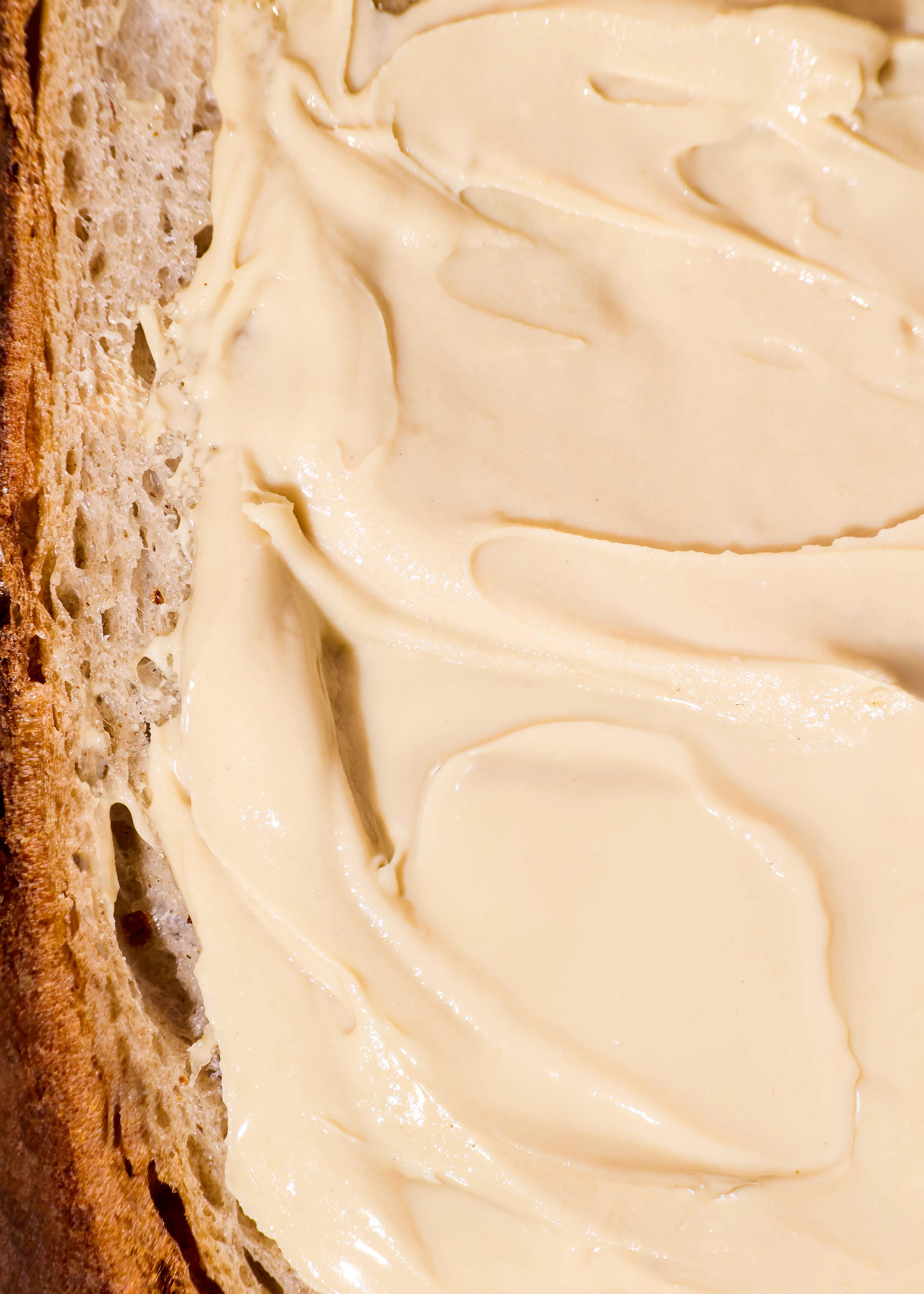 ein nahaufnahme eines stücks brot, bestrichen mit einem hellen, cremigen aufstrich, der wellen aufweist.