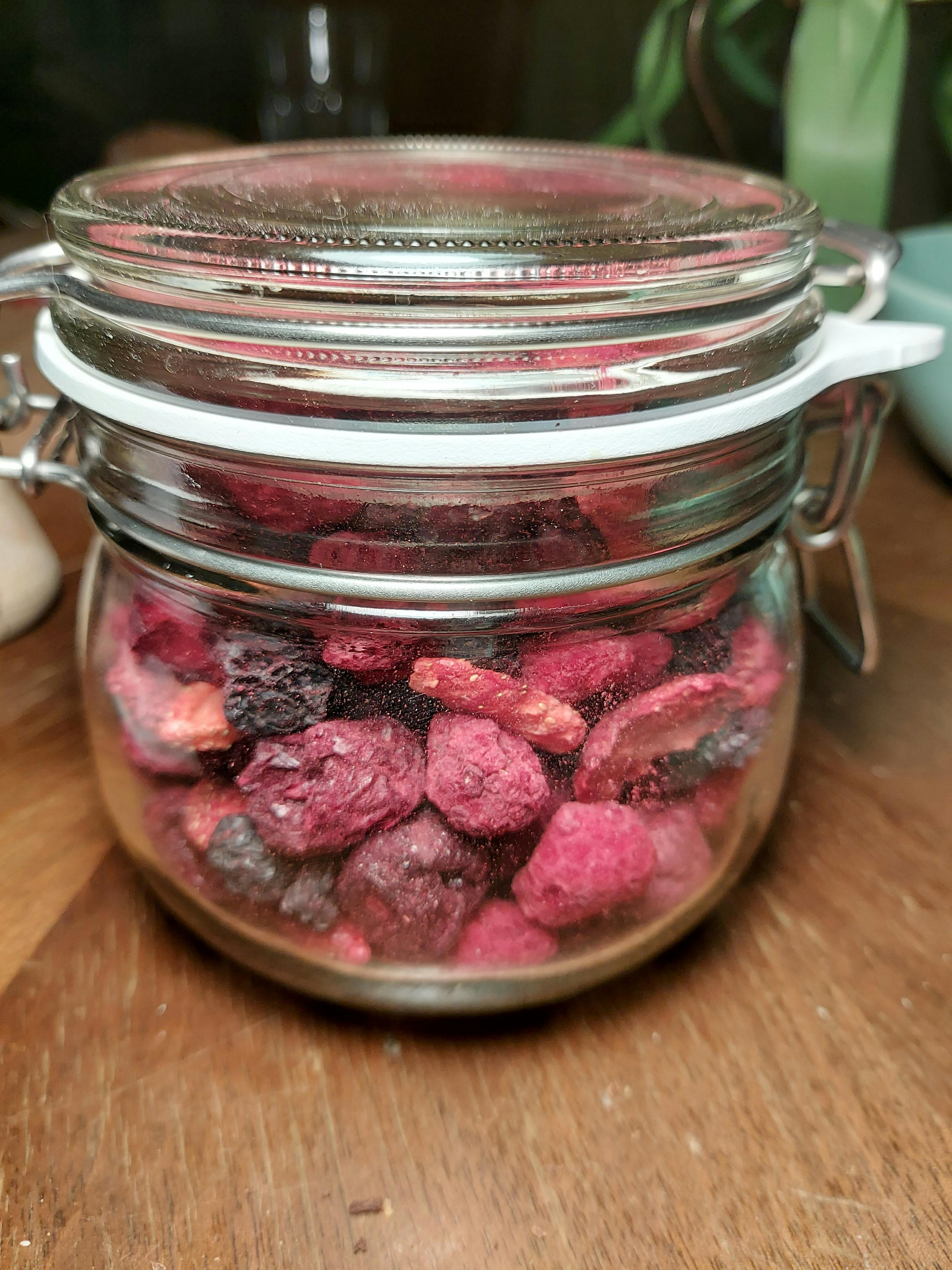 a glass jar filled with dried berries on a wooden table