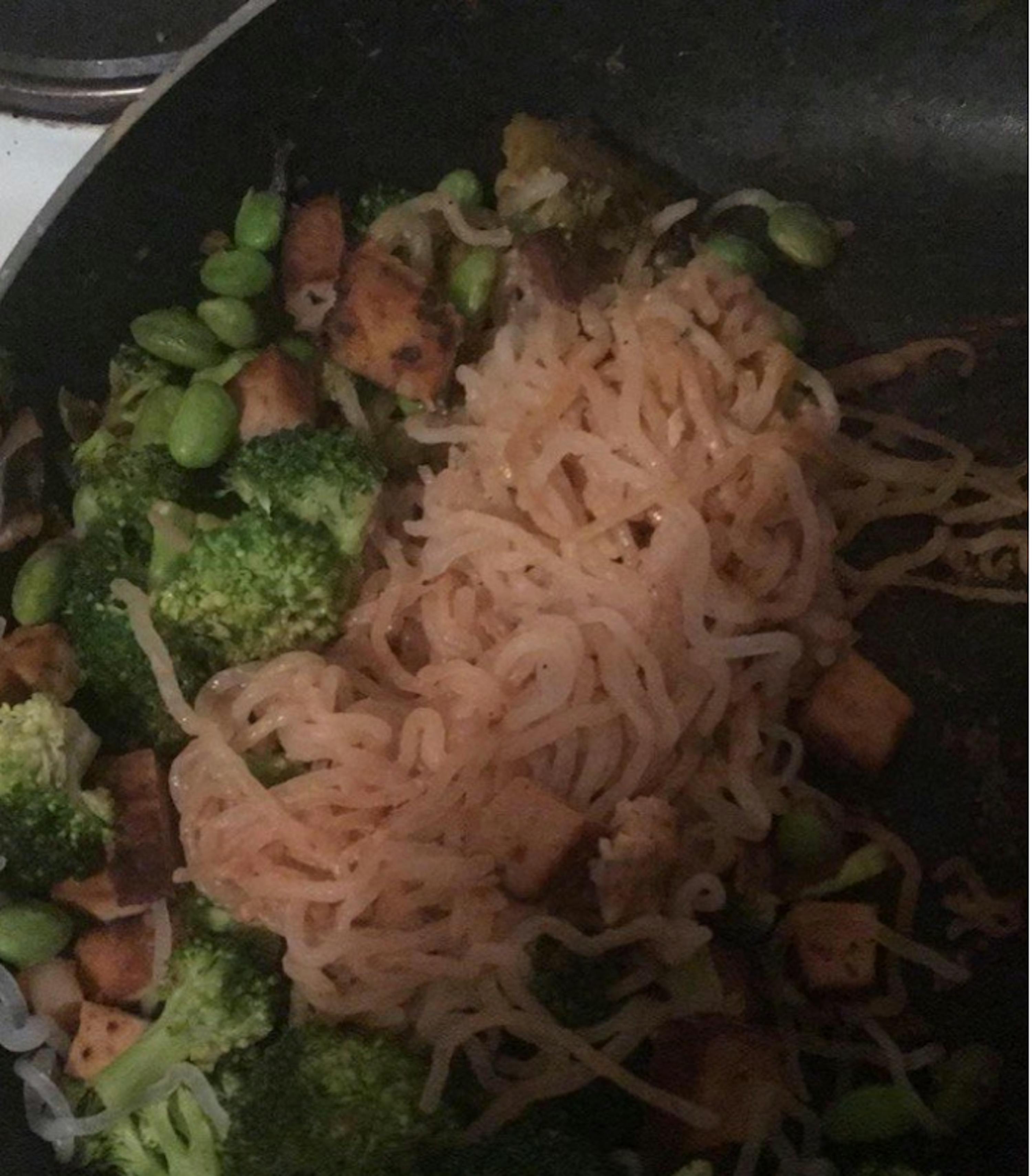 noodles are being added to a stir fry with broccoli and edamame