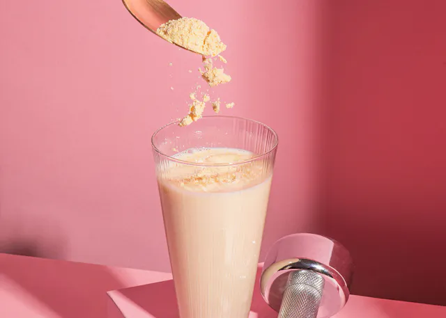 ein Glas Milch wird mit einem Löffelpulver gefüllt