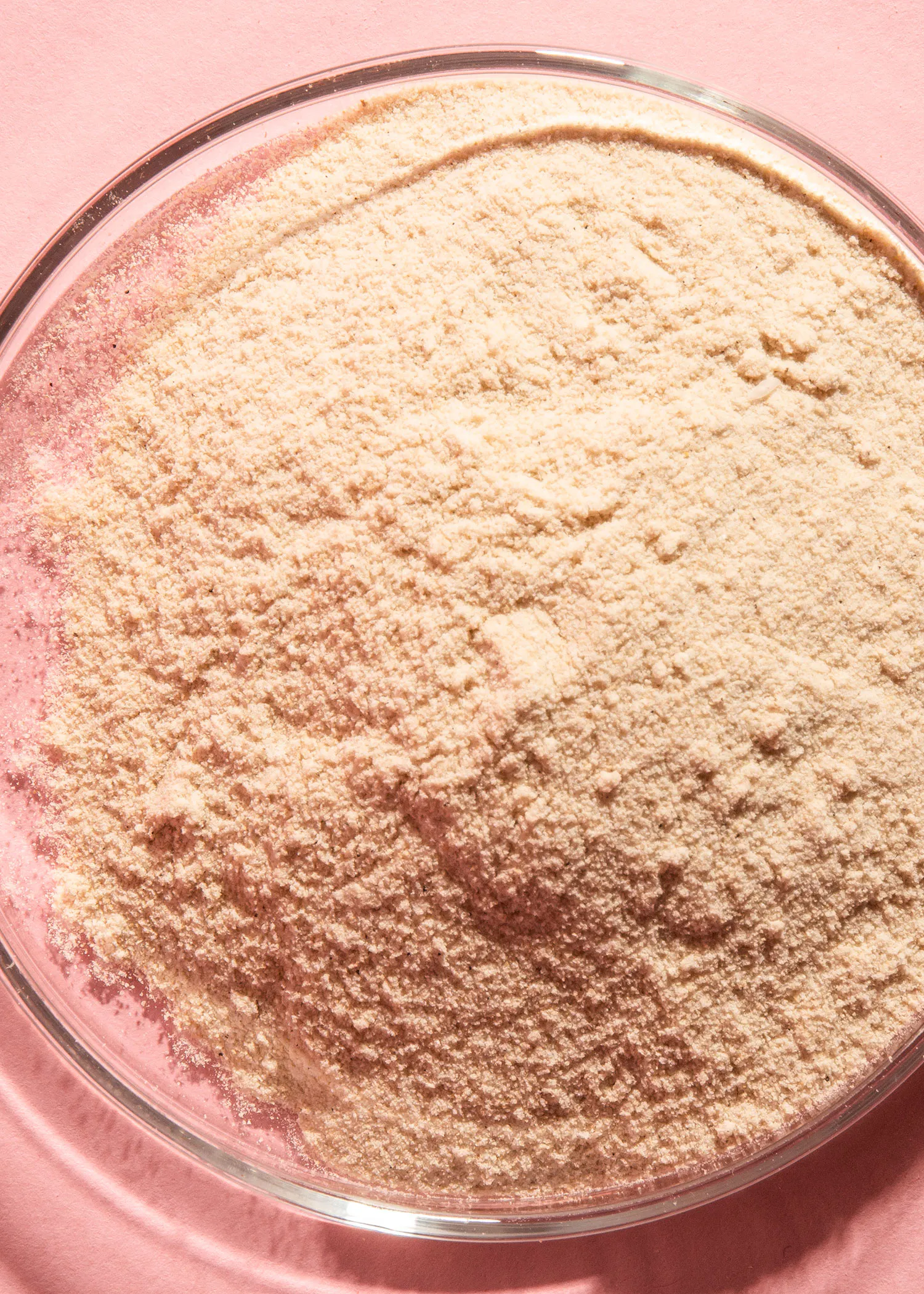 un bol en verre rempli de poudre sur un fond rose