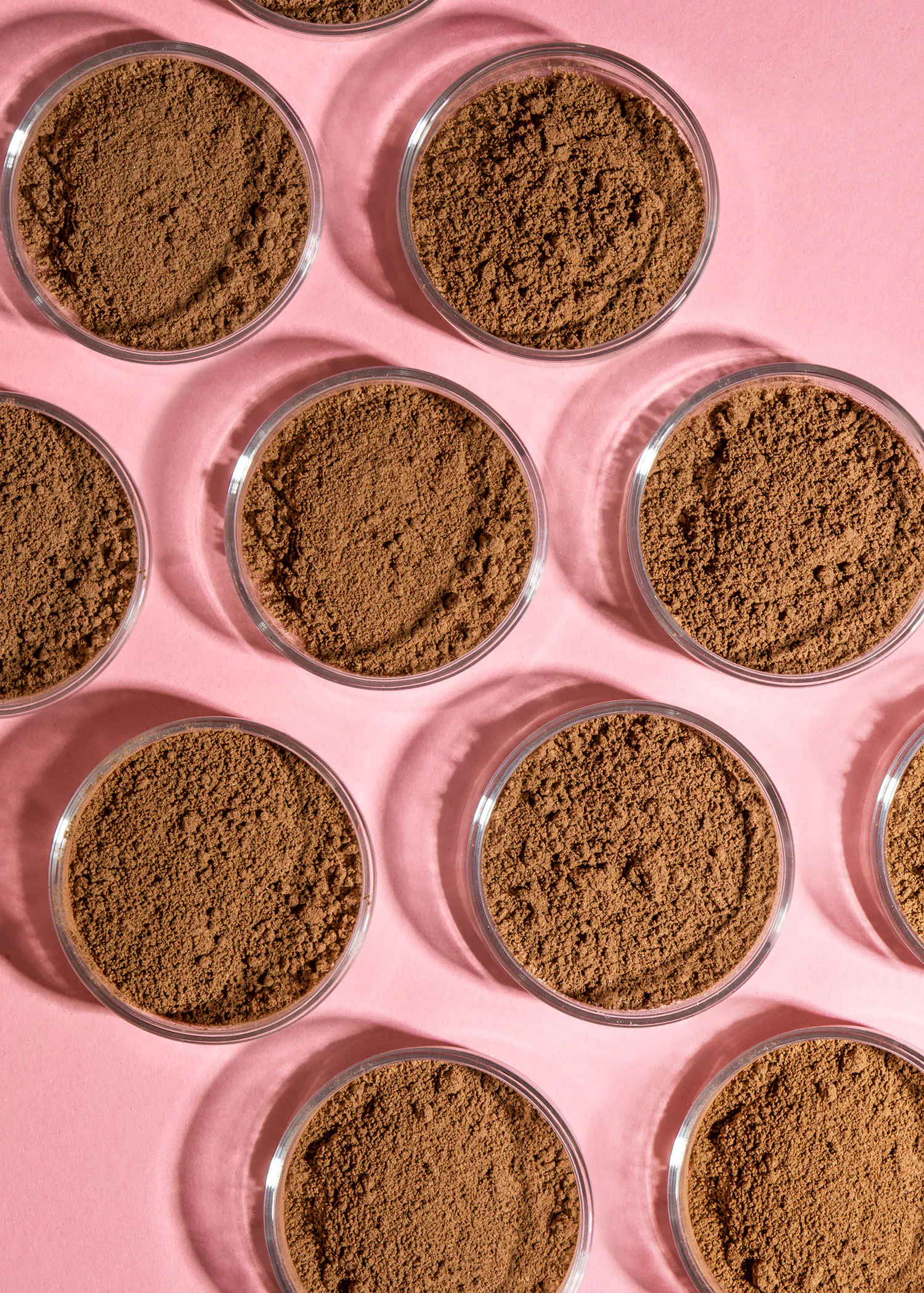 un groupe de bols en verre remplis de poudre brune sur un fond rose