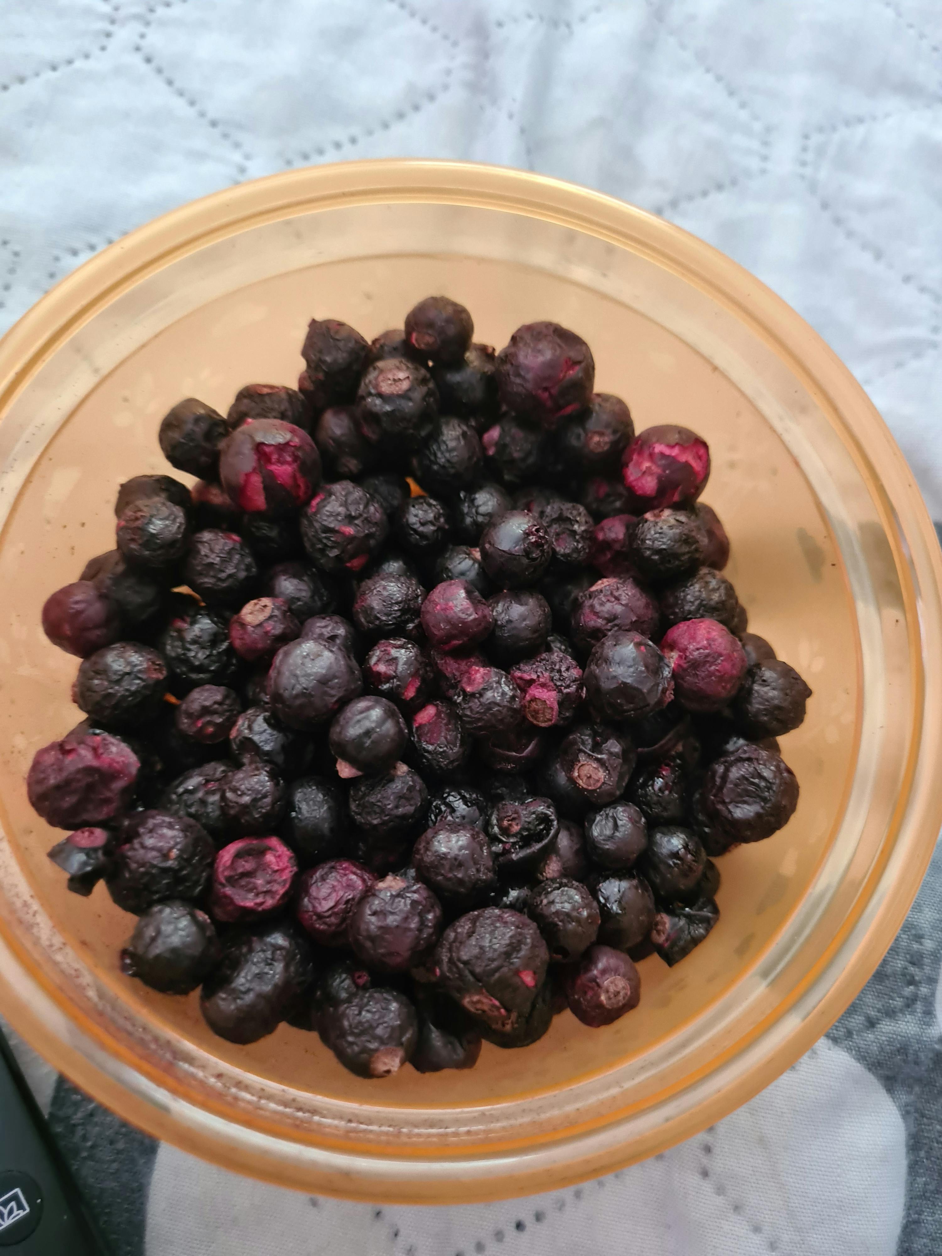a bowl of blueberries sits on a bed next to a remote control