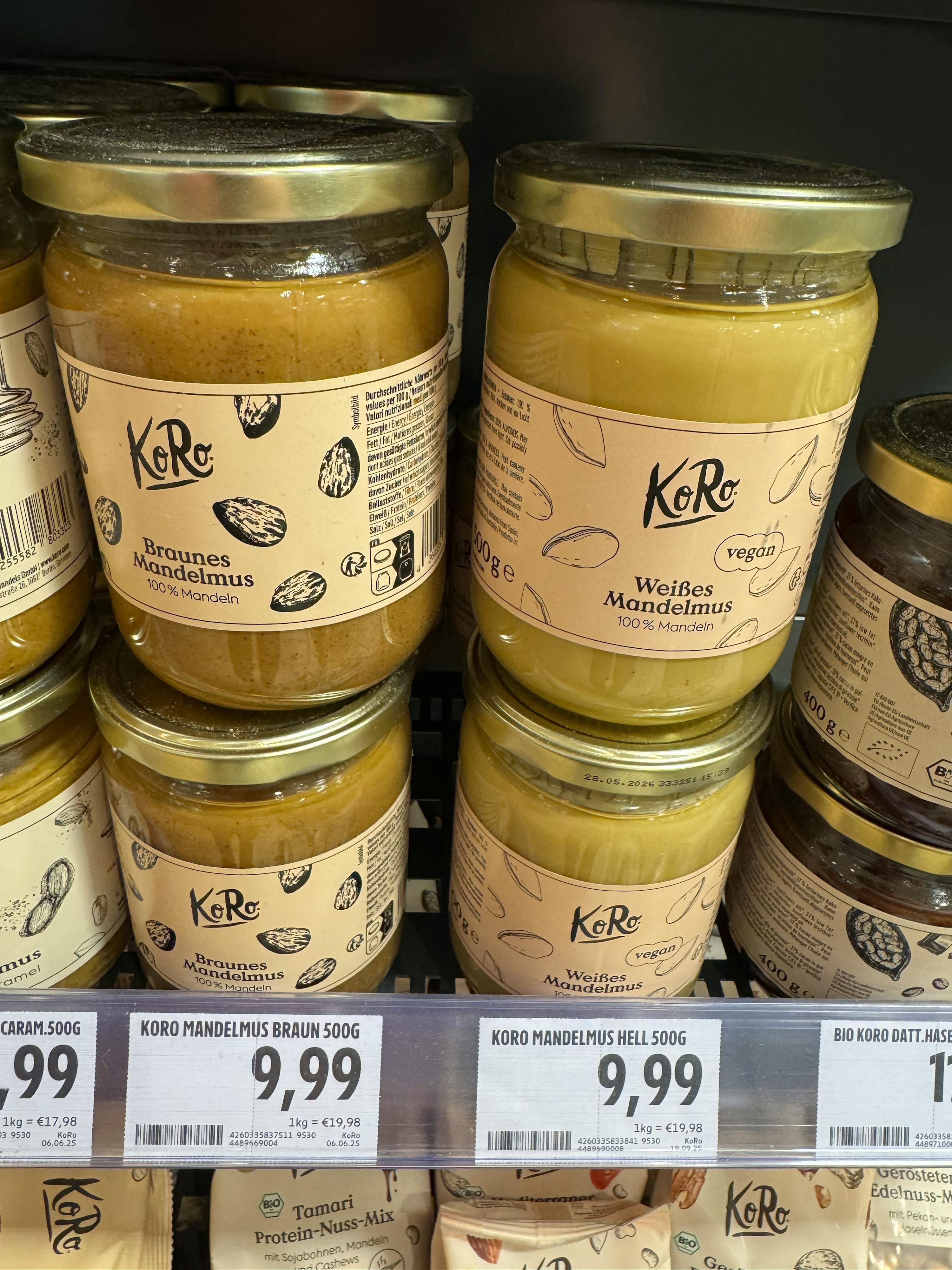 mehrere gläser koro weißes und braunes mandelmus stehen in einem regal mit preisschildern.