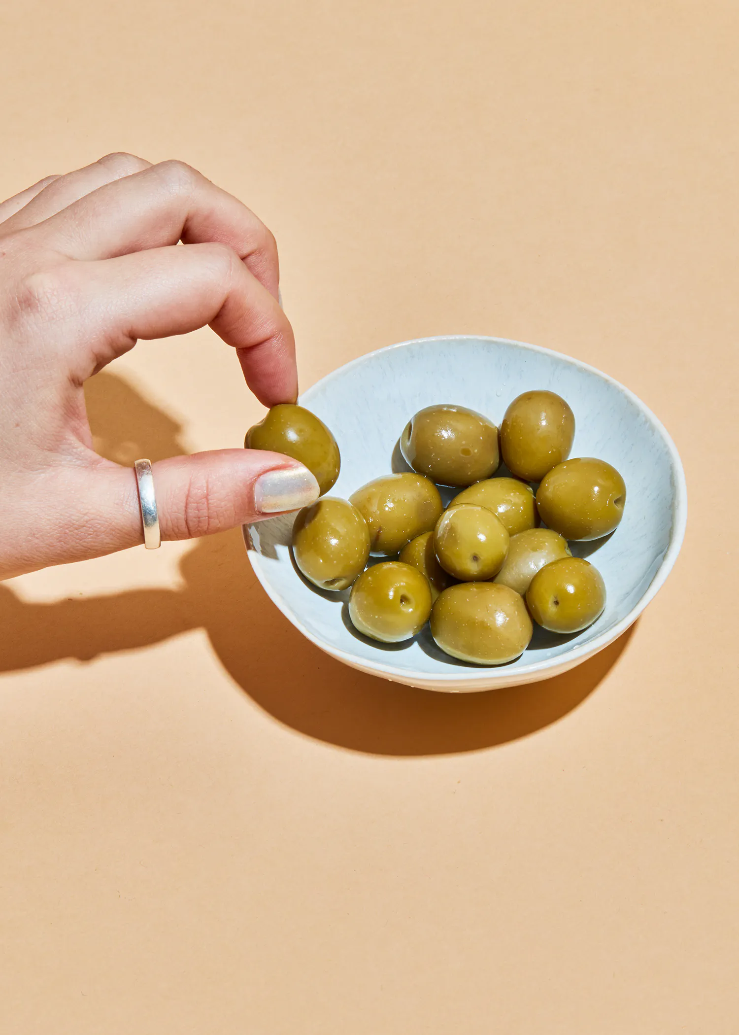 a woman 's hand is reaching for a green olive from a bowl of olives