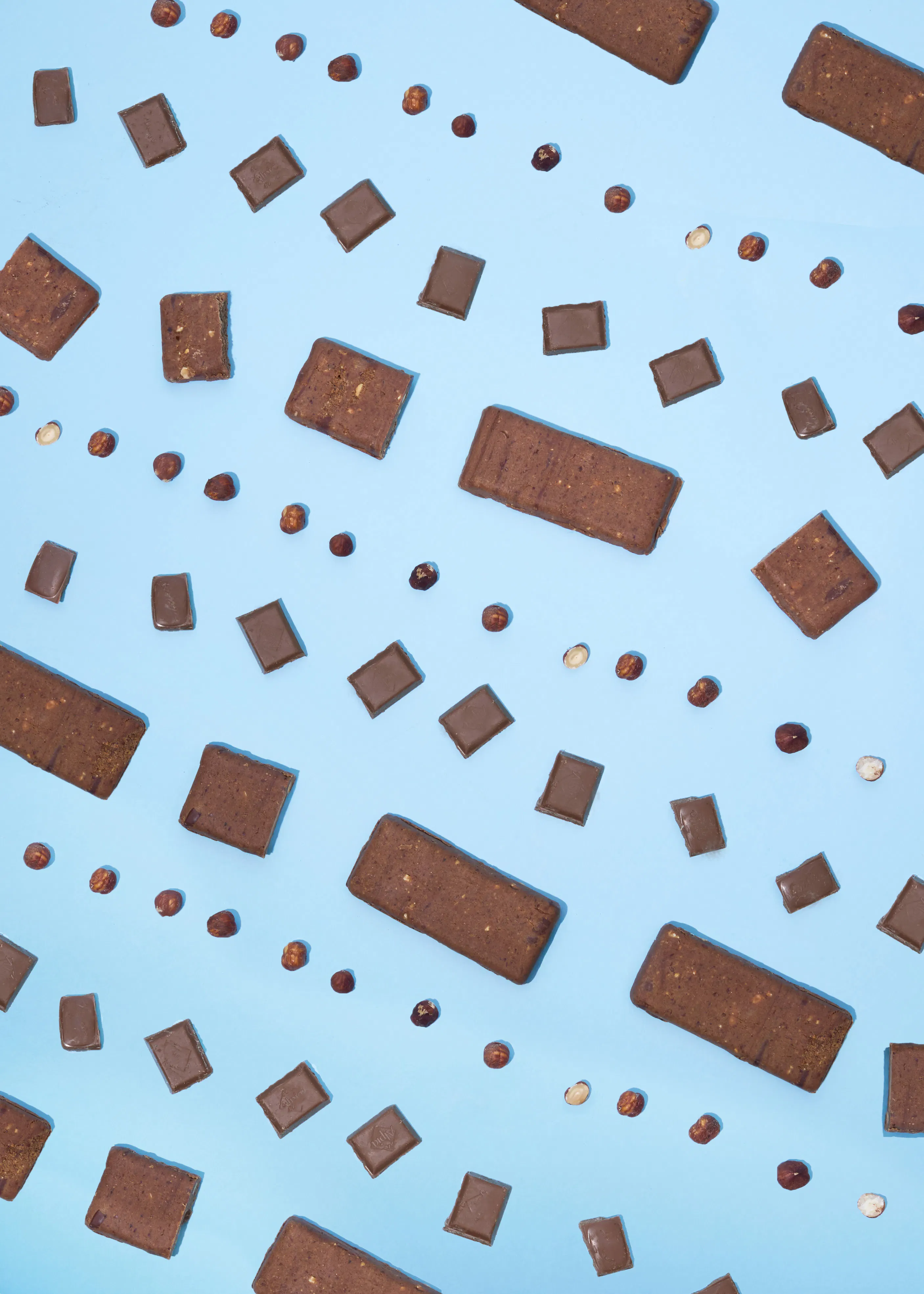 un motif de barres chocolatées, de morceaux de chocolat et de noisettes éparpillés sur un fond bleu clair.