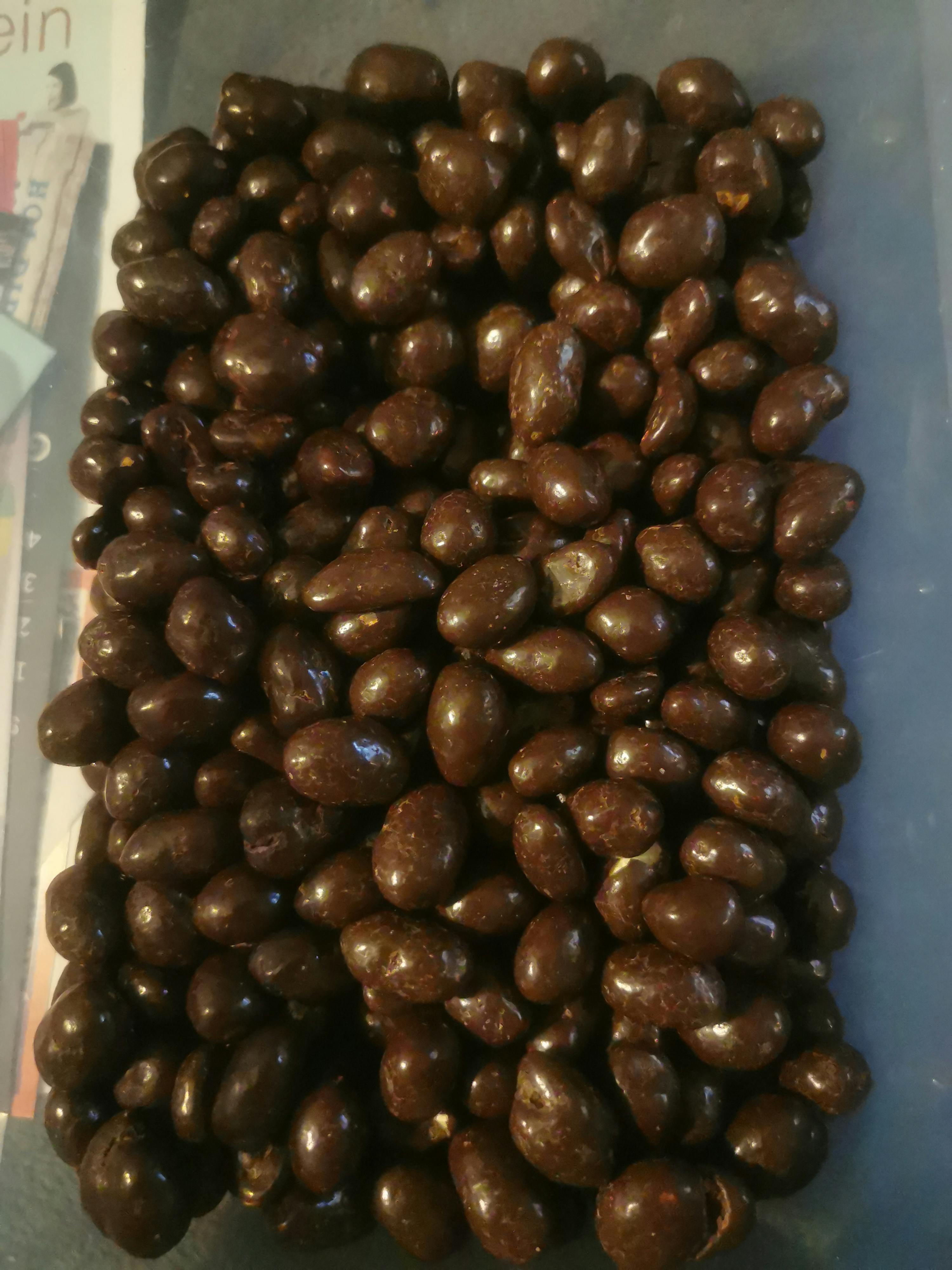 una vista dall'alto di un mucchio di dolcetti scuri e lucidi, probabilmente noci o frutta secca ricoperte di cioccolato.