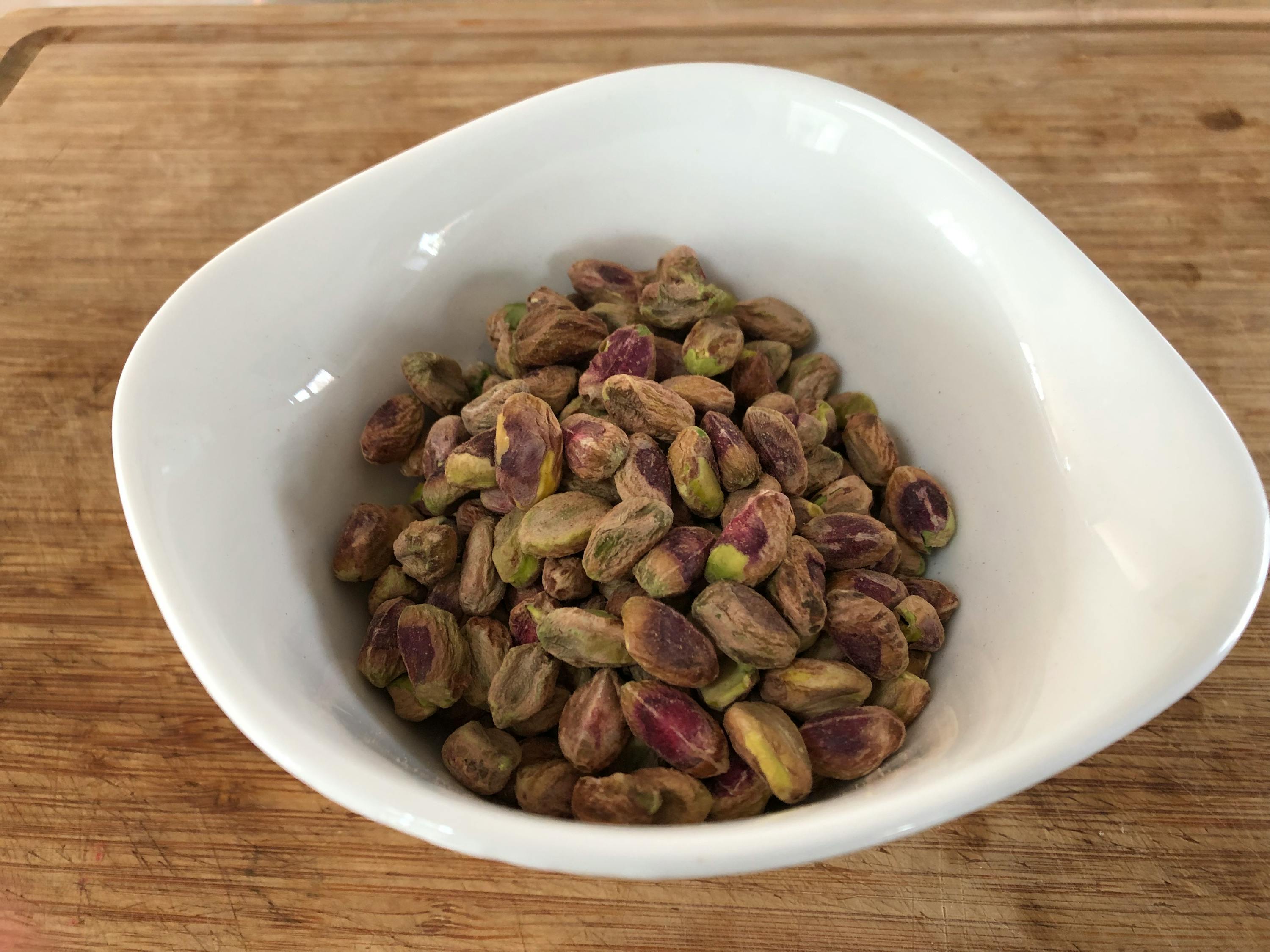 una ciotola bianca piena di pistacchi è su un tagliere di legno