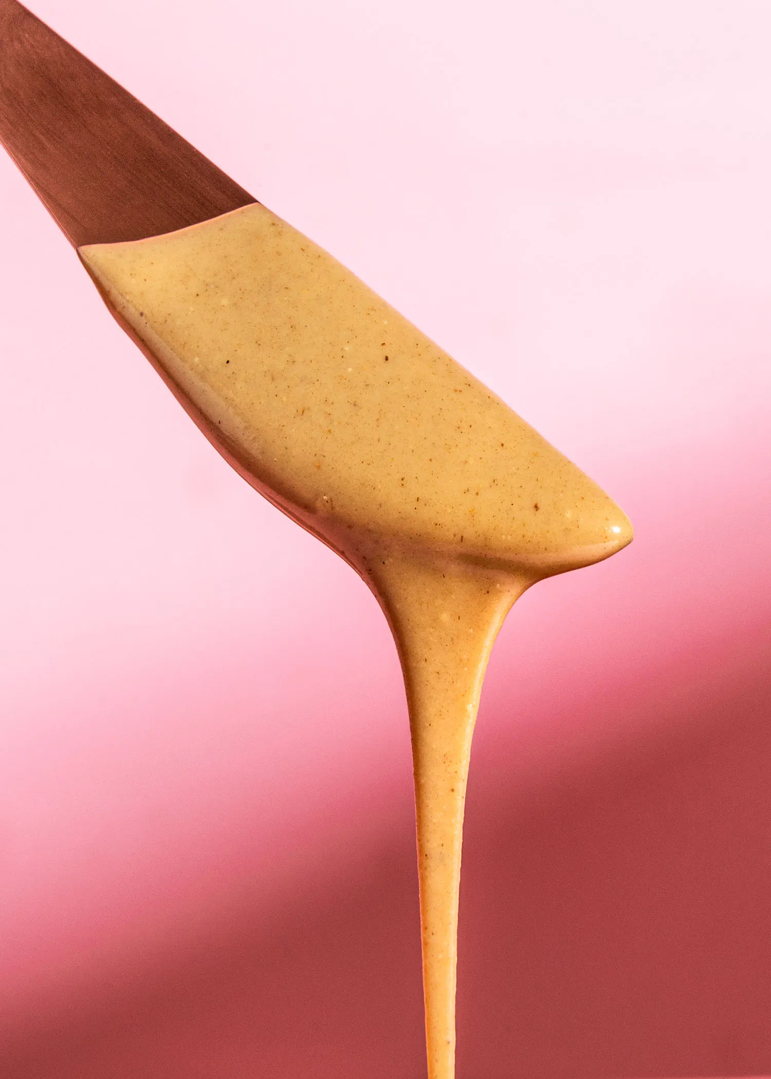 une cuillère en bois remplie de sauce sur fond rose