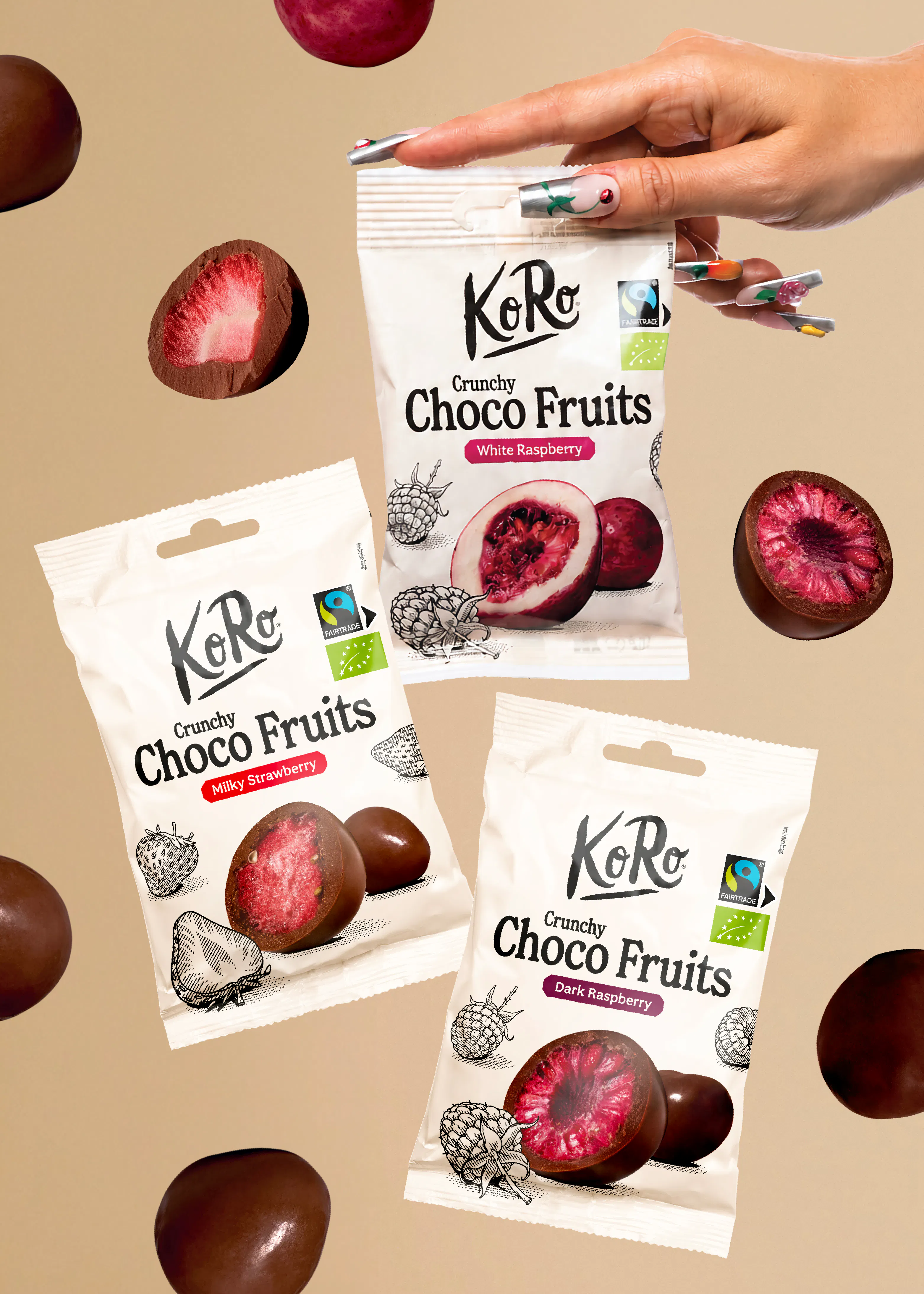 une main tient un sachet de fruits enrobés de chocolat koro entouré de plusieurs autres sachets et de fruits chocolatés flottant sur un fond beige.