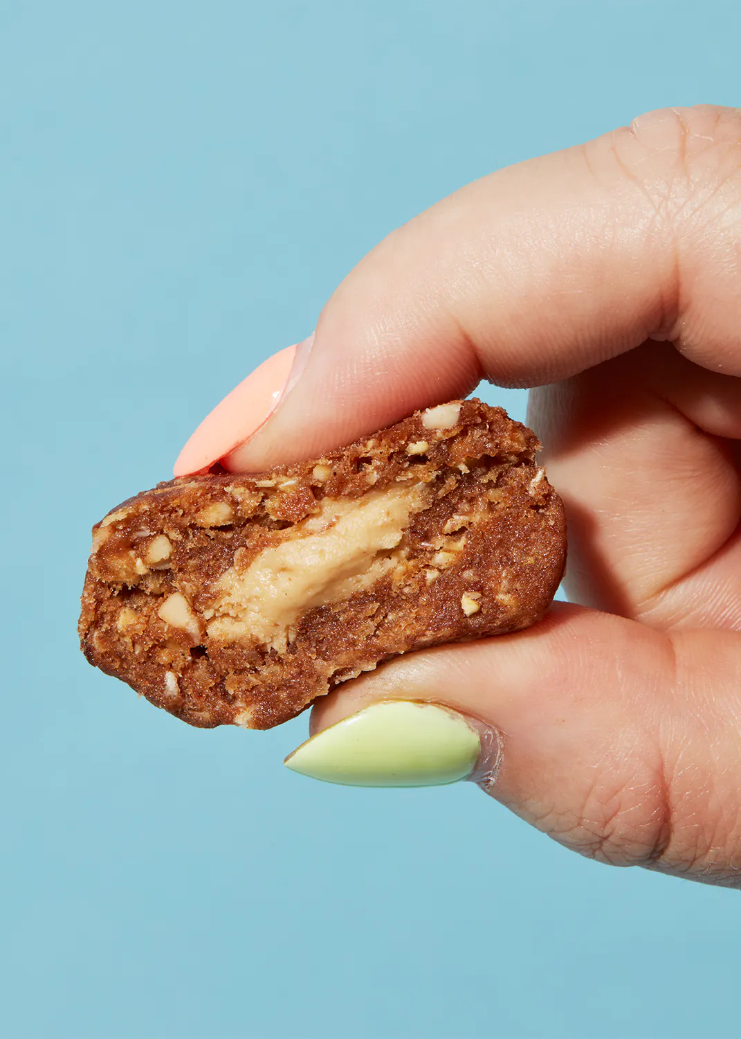 eine Person mit grünen Nägeln hält einen Keks mit Erdnussbutter darin