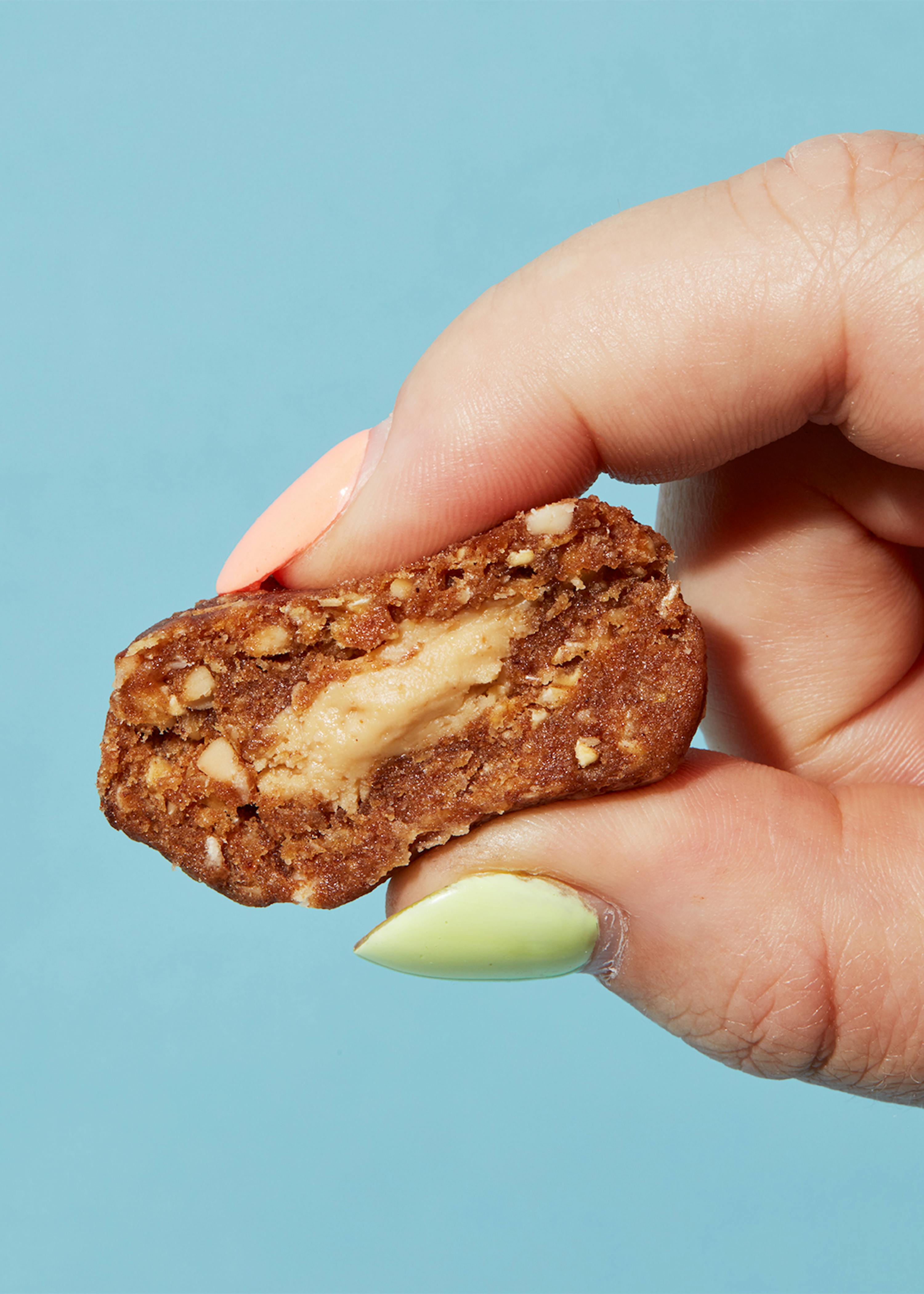 eine Person mit grünen Nägeln hält einen Keks mit Erdnussbutter darin