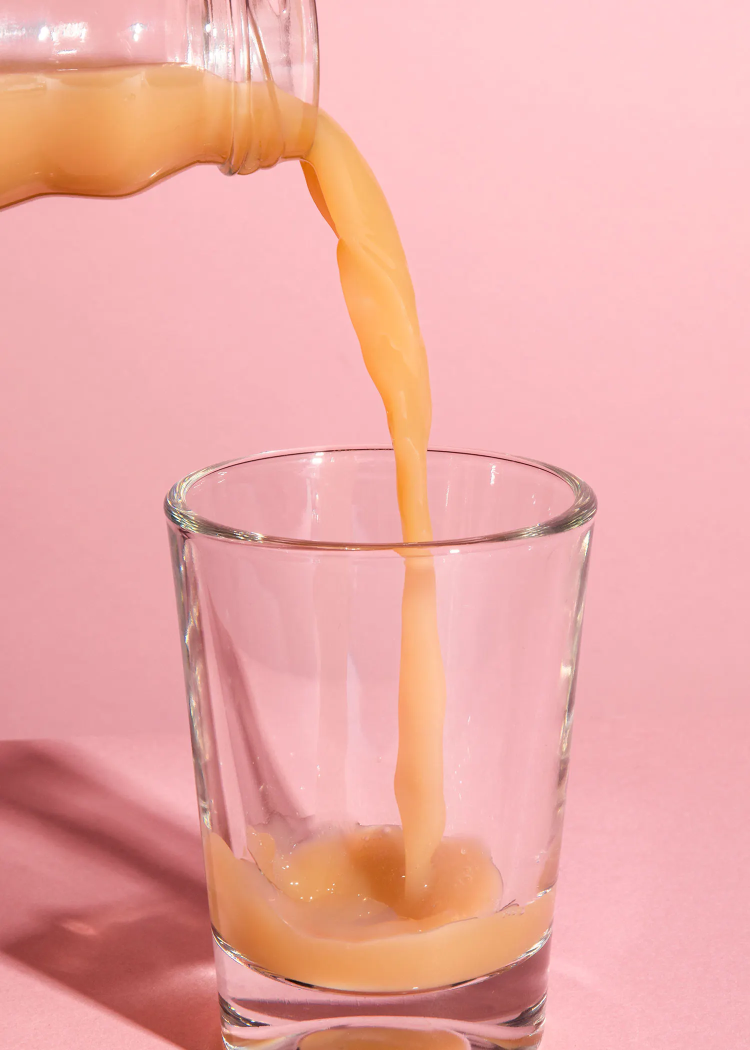 un liquide est versé dans un verre sur fond rose