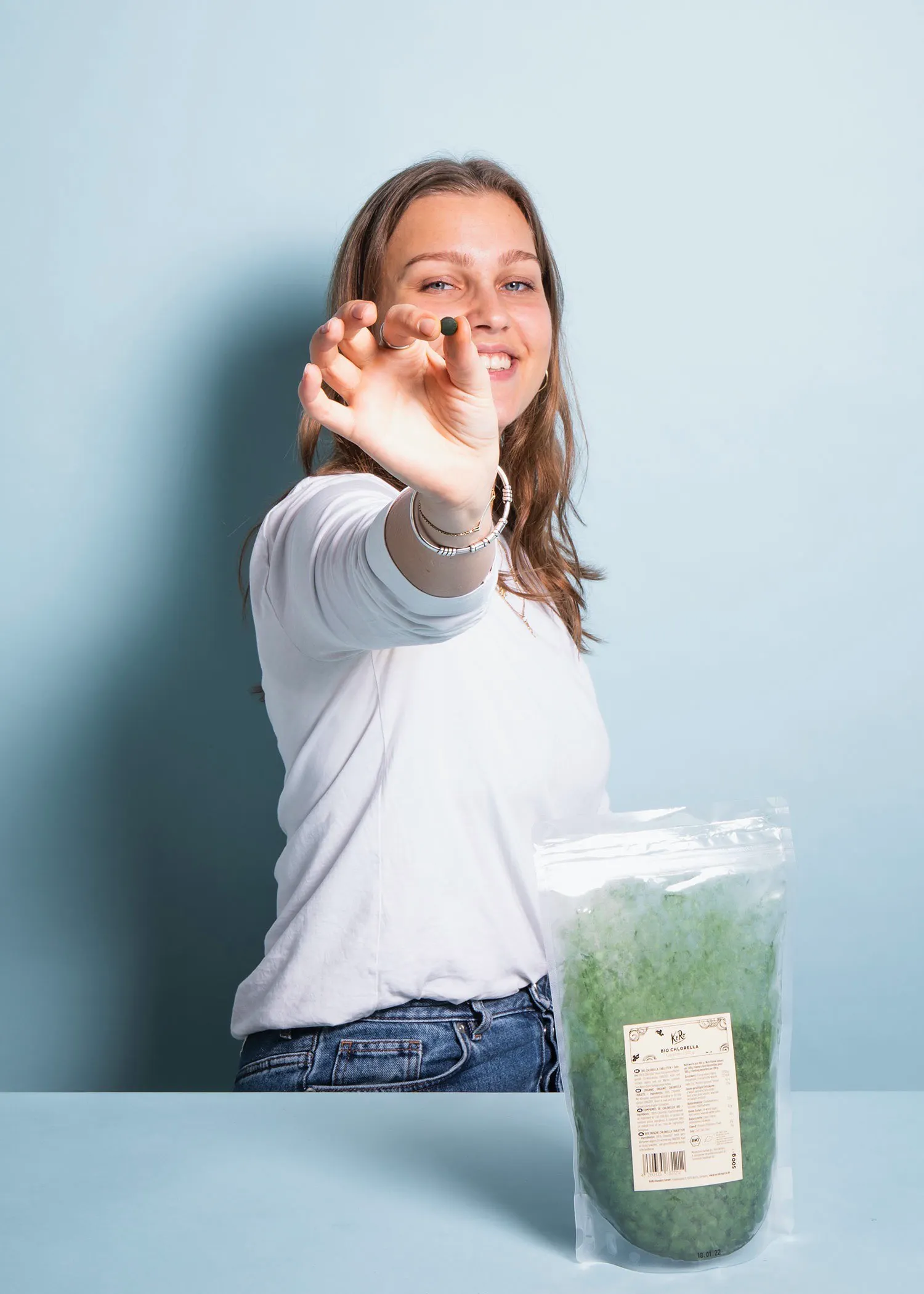 une femme tient une pilule dans sa main à côté d' un sac d' algues