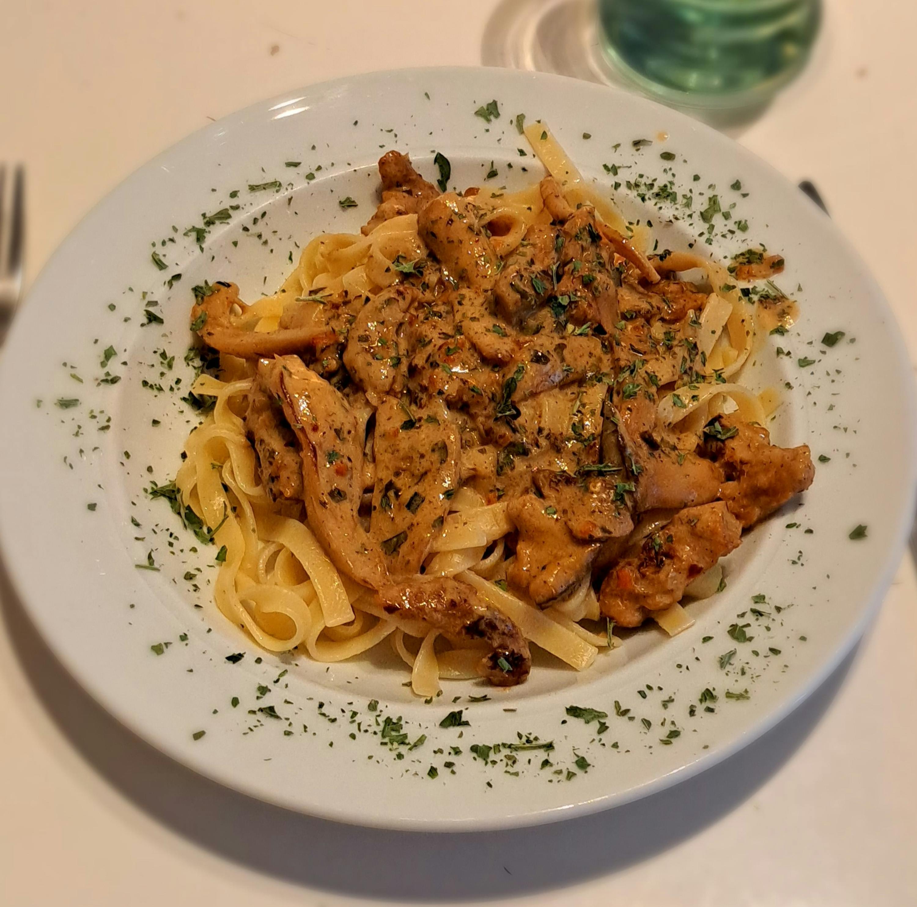 ein weißer Teller mit Nudeln und Fleisch auf einem Tisch