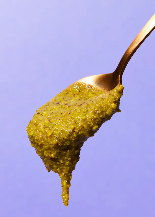 a spoon filled with a green sauce on a purple background