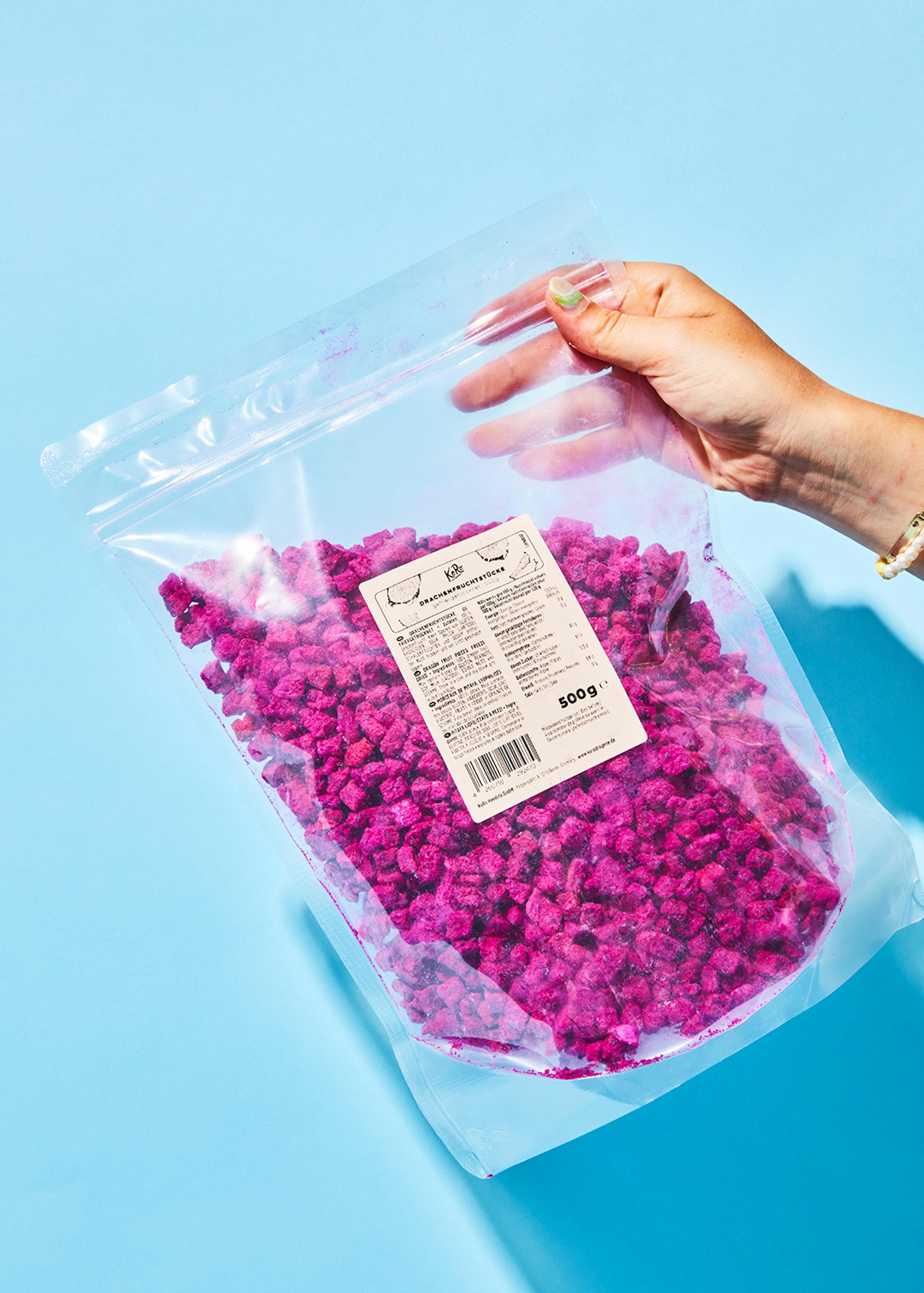 une personne tient un sac en plastique rempli de fruits roses