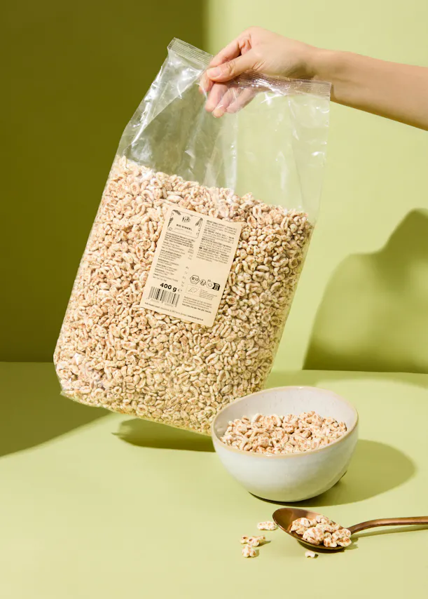 eine Person hält eine Tüte Haferflocken neben einer Schüssel Haferflocken und einem Löffel Haferflocken