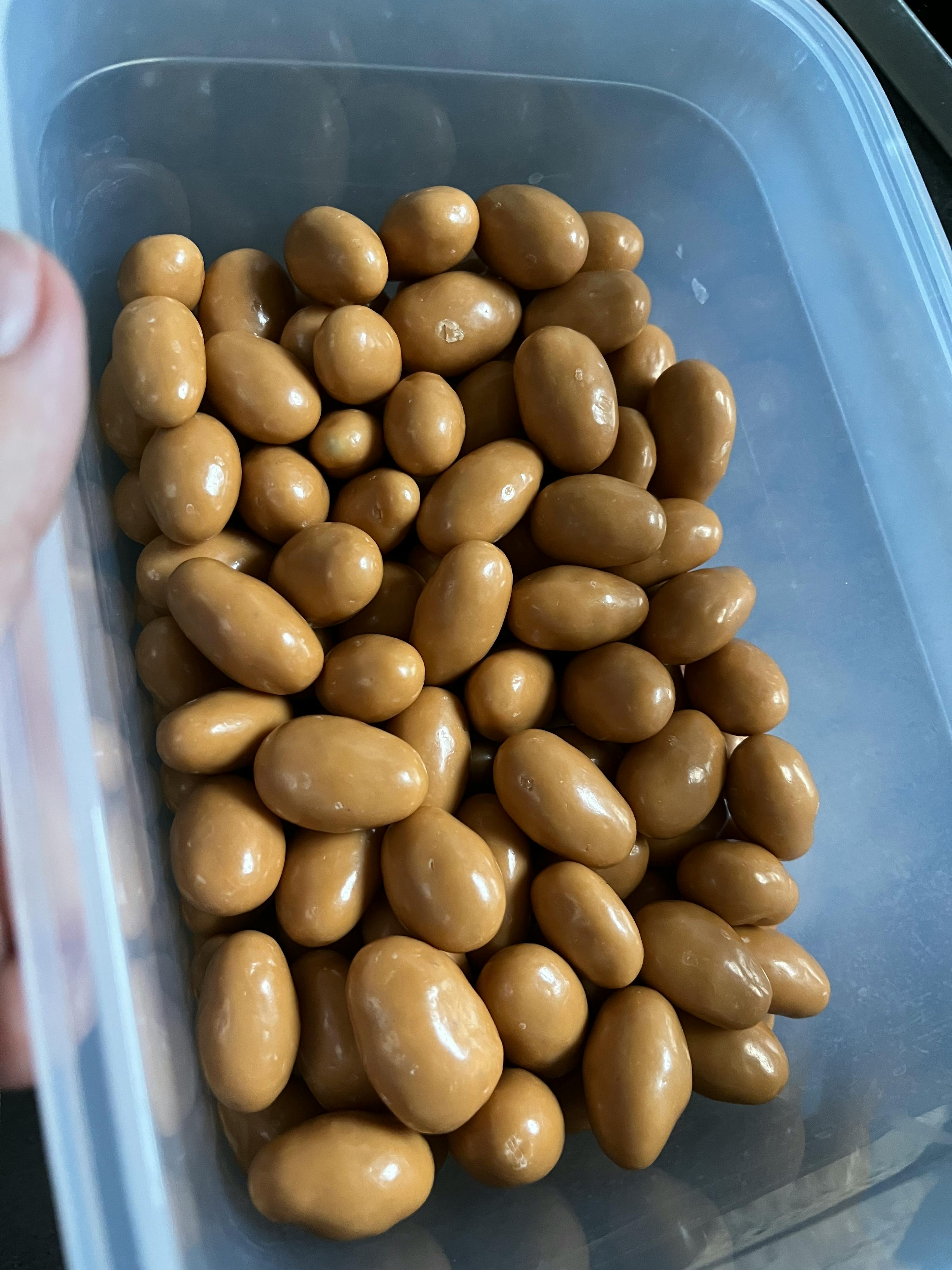 une personne tient une boîte en plastique remplie d' amandes enrobées de caramel