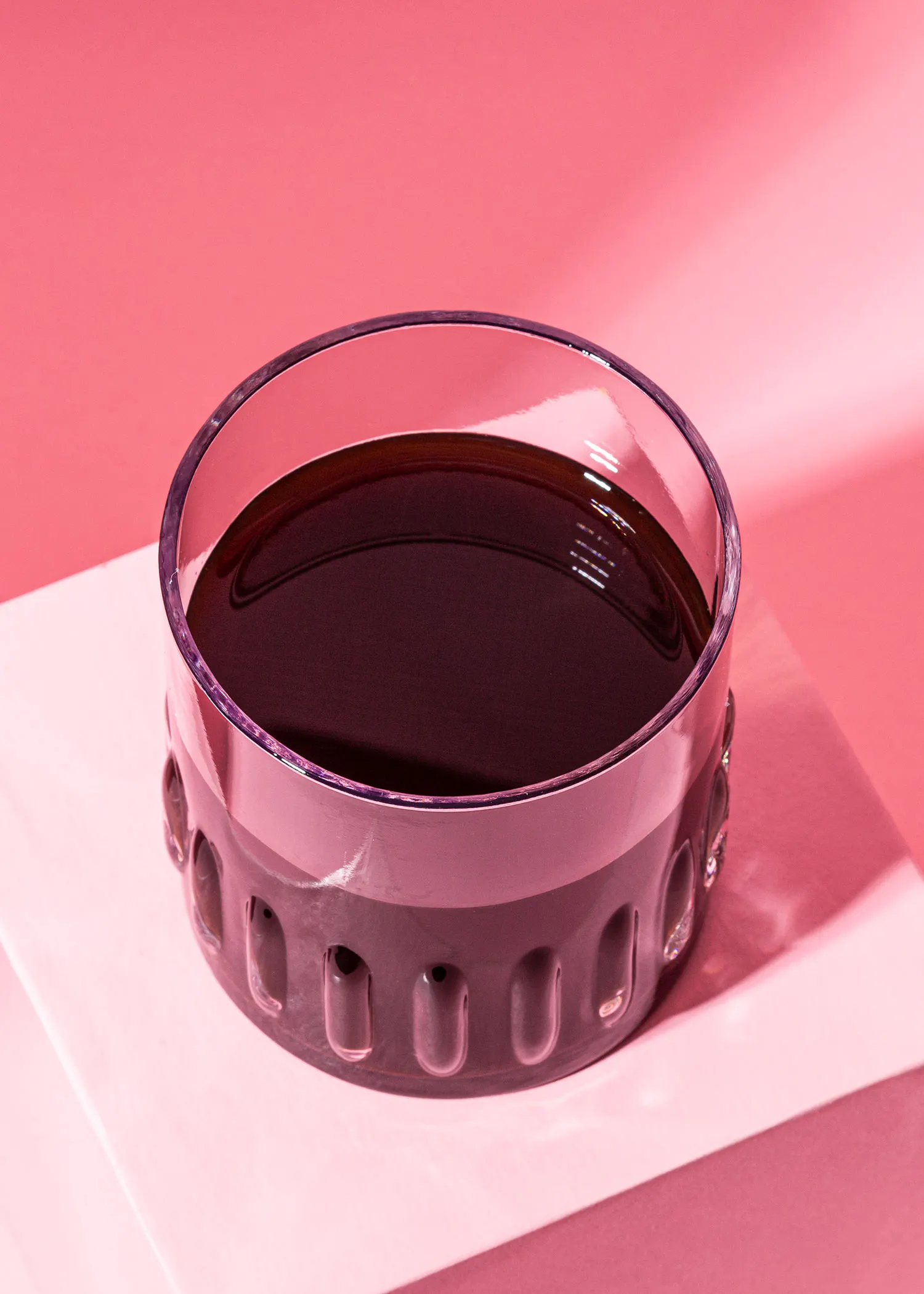 un bol en verre rempli d' un liquide sombre sur une table rose