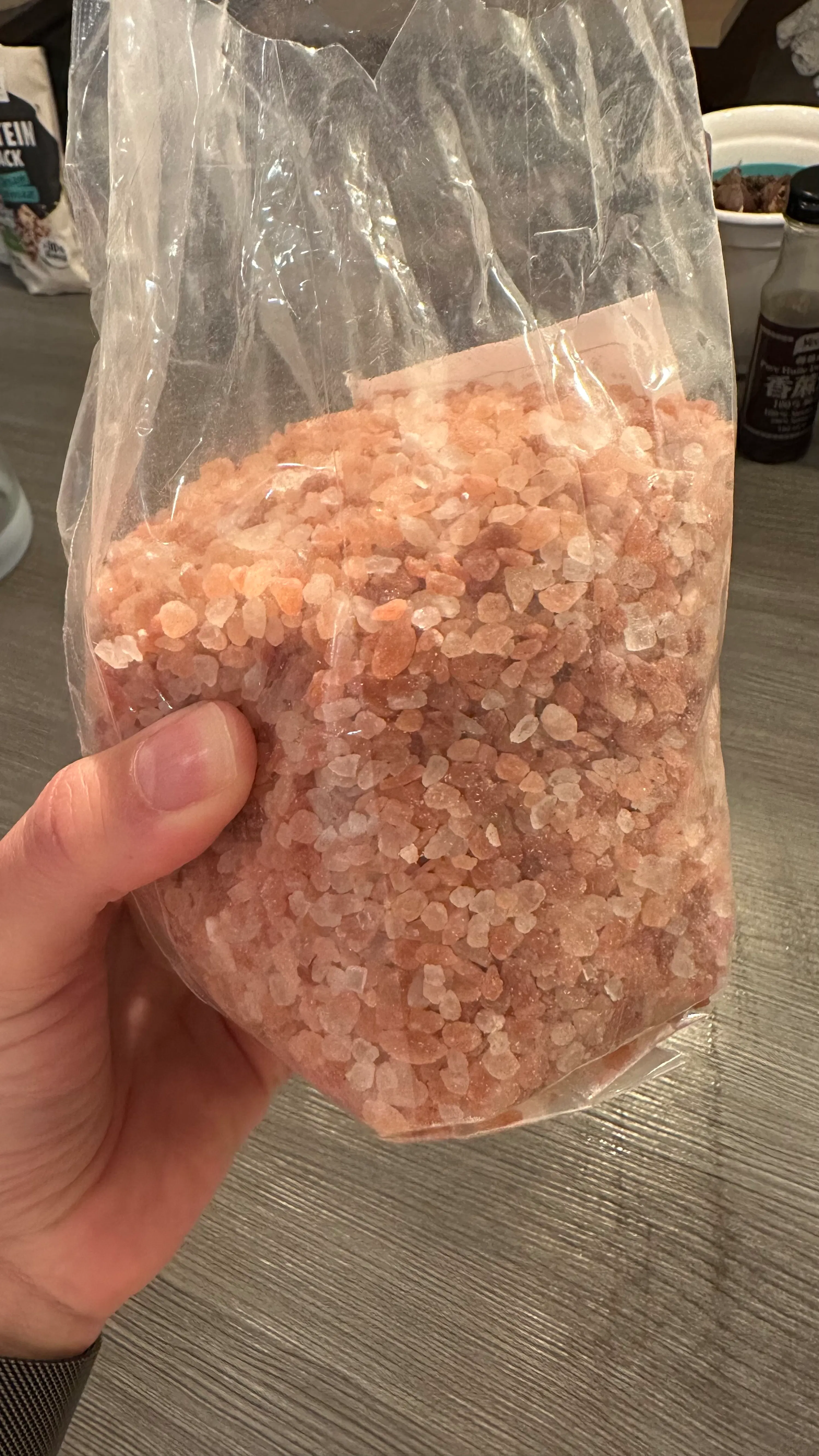 une main tient un sac en plastique transparent rempli de cristaux de sel rose de l'himalaya.