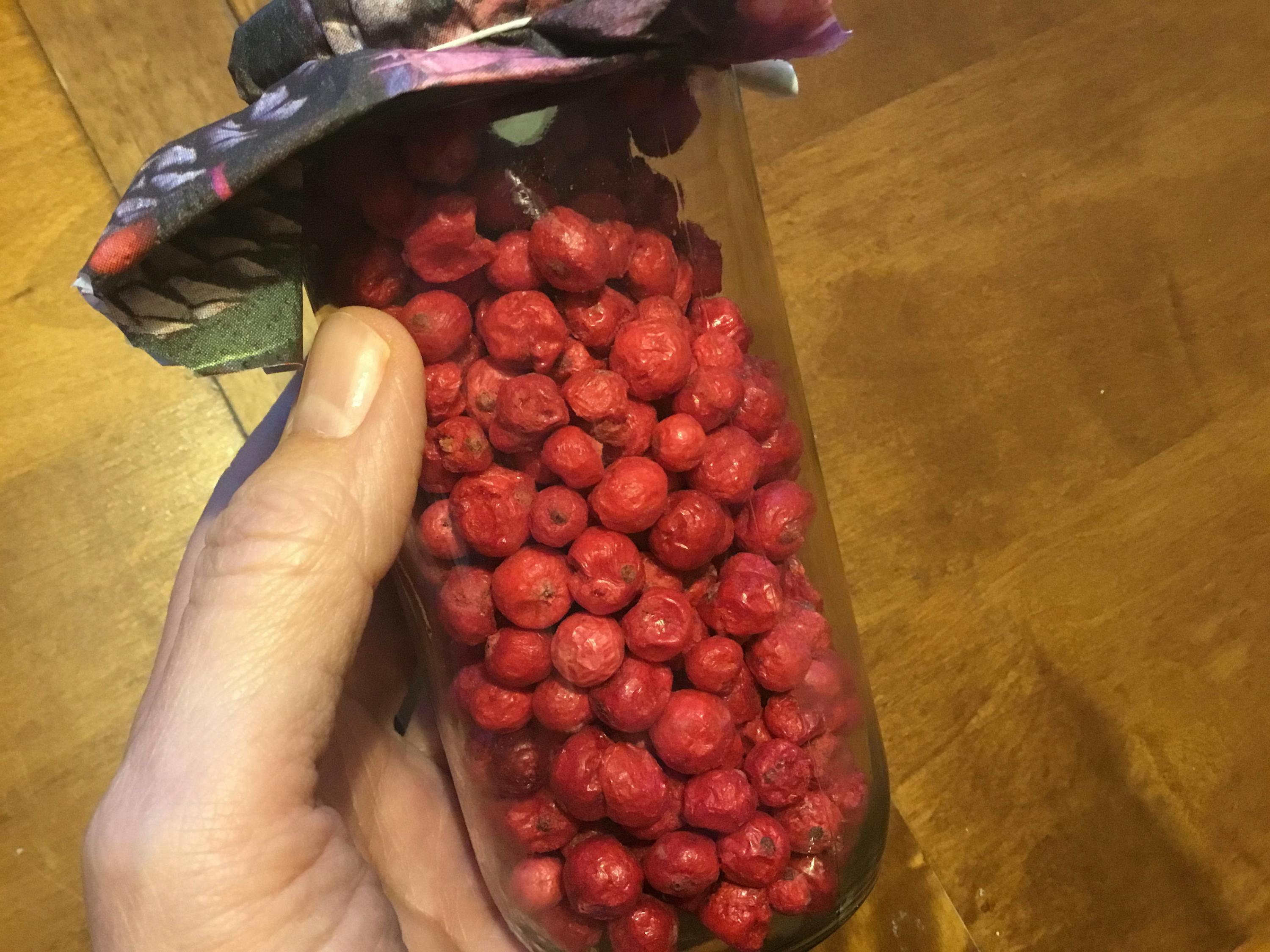 a hand is holding a glass jar filled with red berries