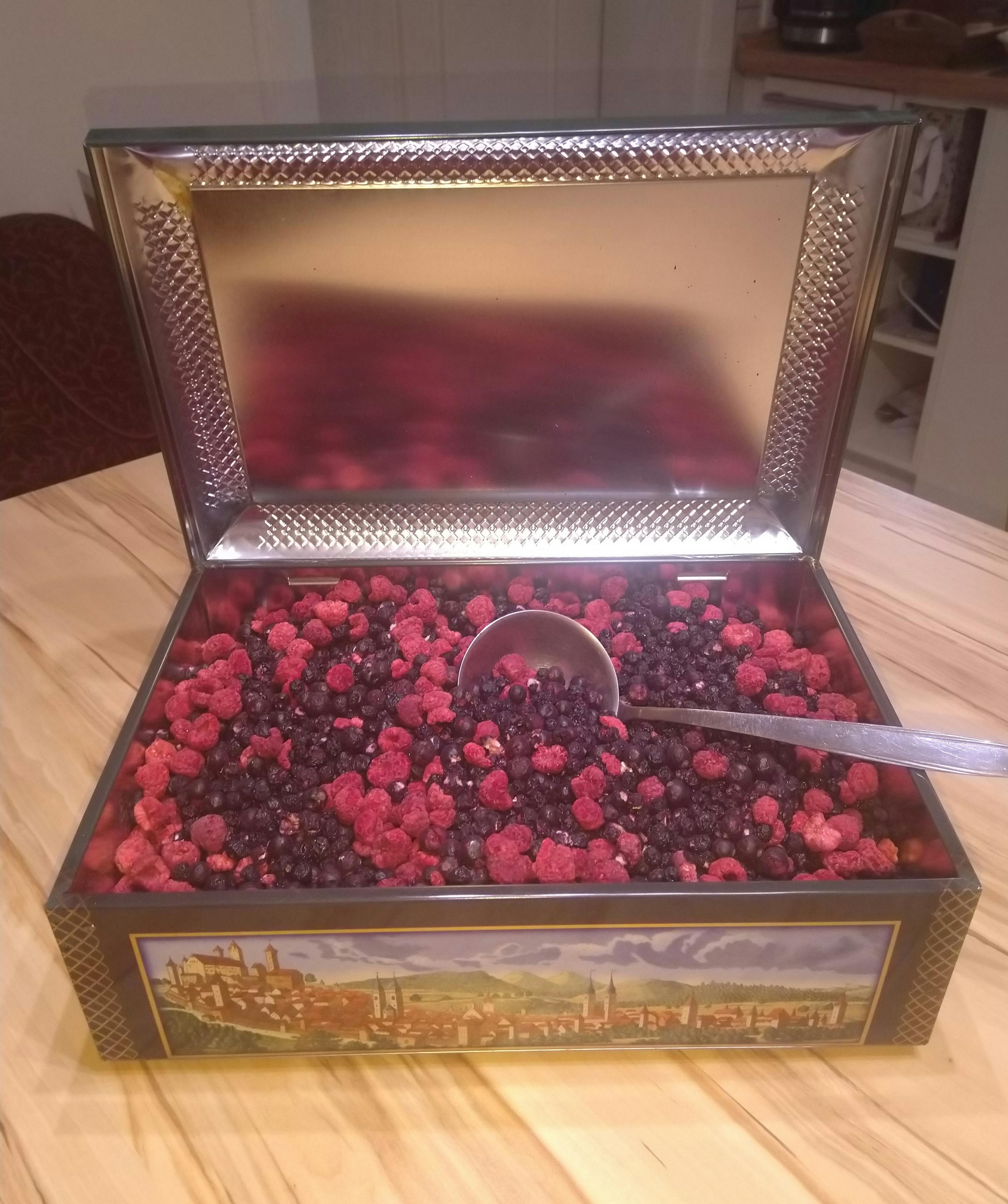 une boîte remplie de baies et de framboises avec une cuillère à l' intérieur