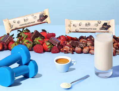 Twee chocoladerepen, twee halters en een glas melk staan op een tafel. Daarachter ligt een rij stukjes chocolade, aardbeien en hazelnoten.