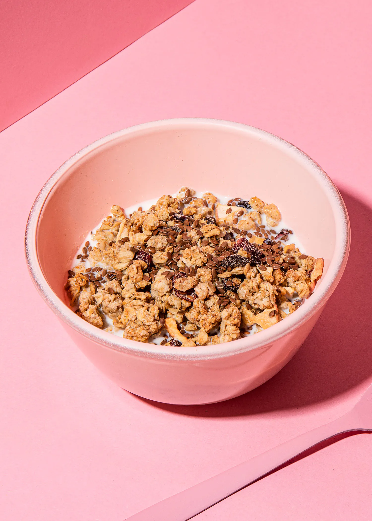 un bol rose rempli de céréales et de lait sur un fond rose