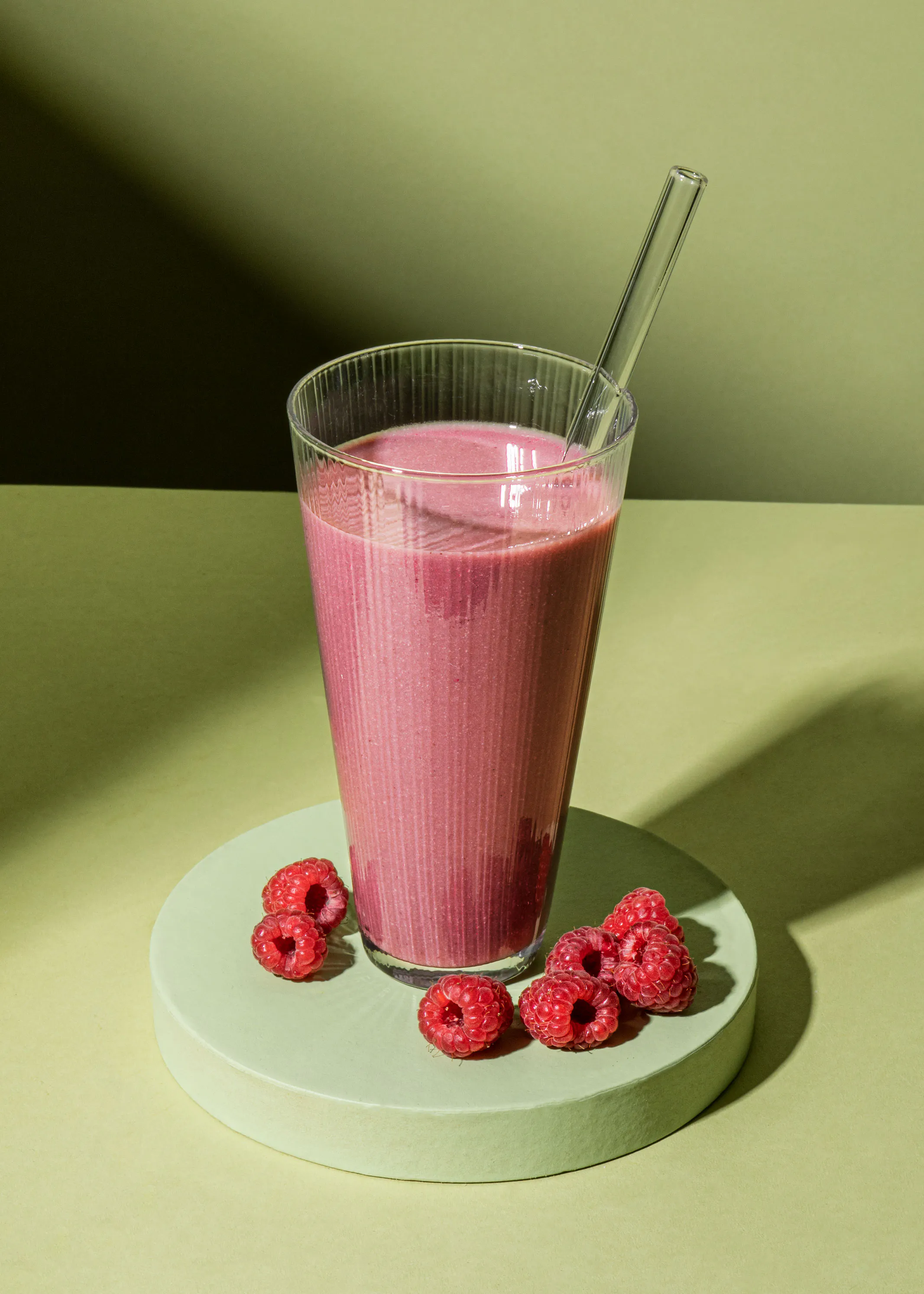 un smoothie rose avec une paille et des framboises à côté