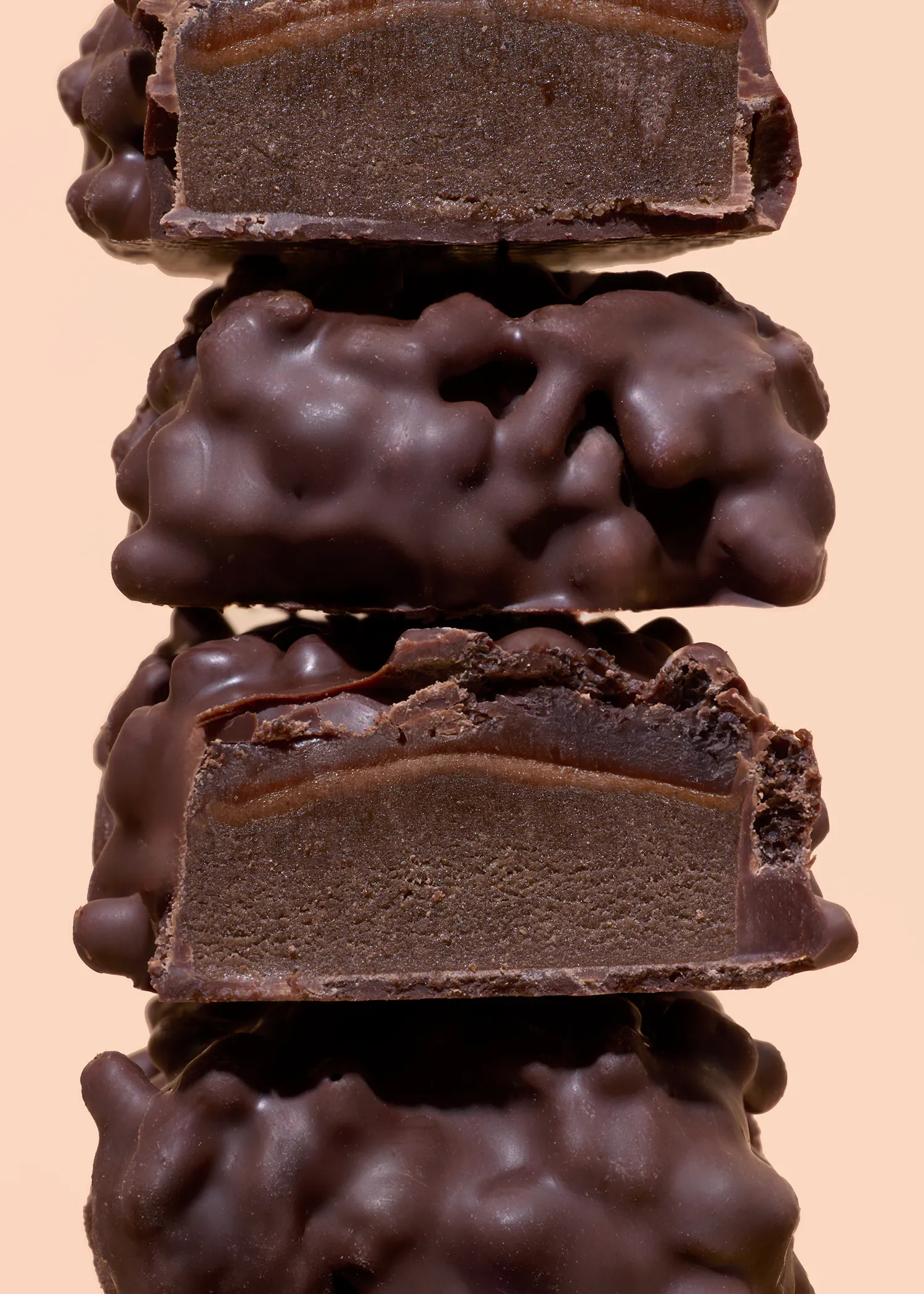 une pile de quatre bonbons au chocolat, dont deux coupés en deux, révélant une garniture au chocolat noir et une couche de caramel sous un enrobage de chocolat bosselé.