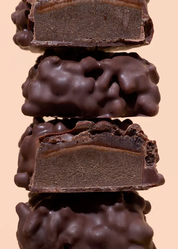 une pile de quatre bonbons au chocolat, dont deux coupés en deux, révélant une garniture au chocolat noir et une couche de caramel sous un enrobage de chocolat bosselé.