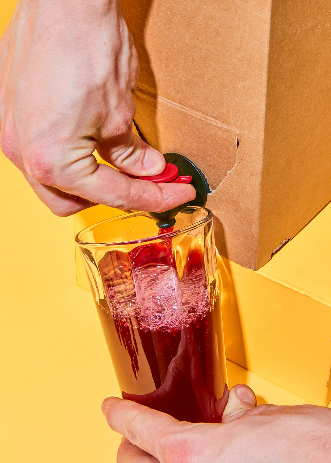 une personne verse une boisson rouge dans un verre
