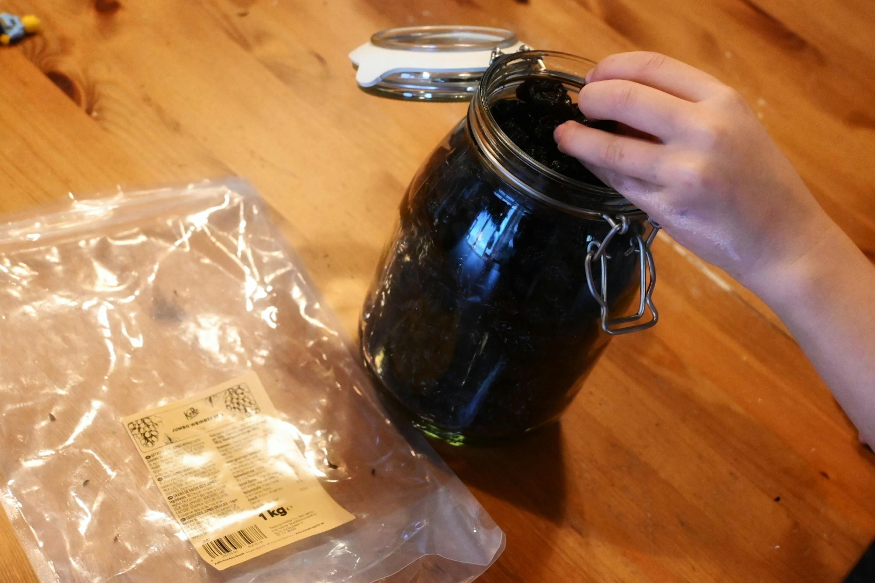 eine Person füllt einen Glasbehälter mit einem Plastikbeutel auf einem Holztisch