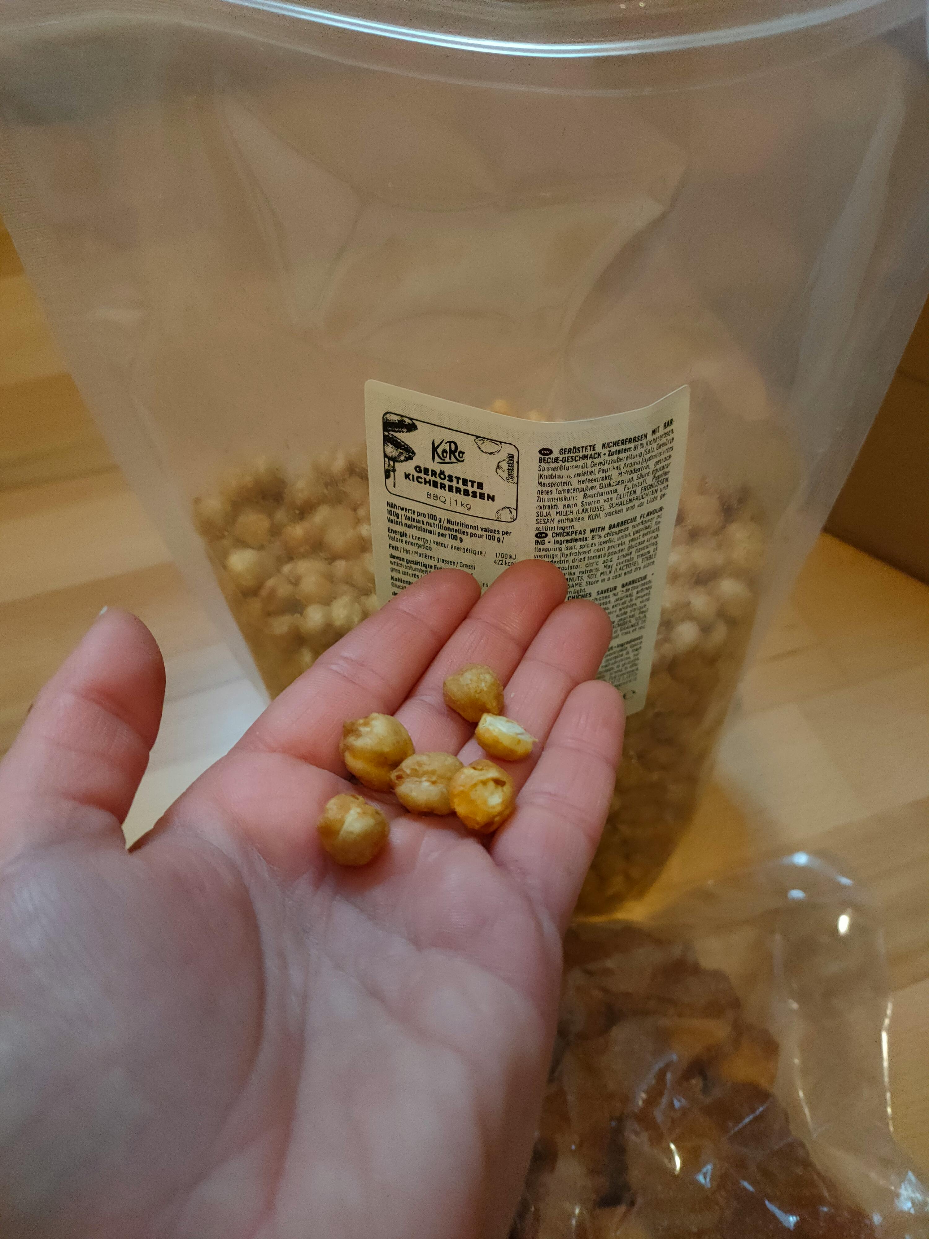 a person is holding a handful of nuts in front of a container of nuts